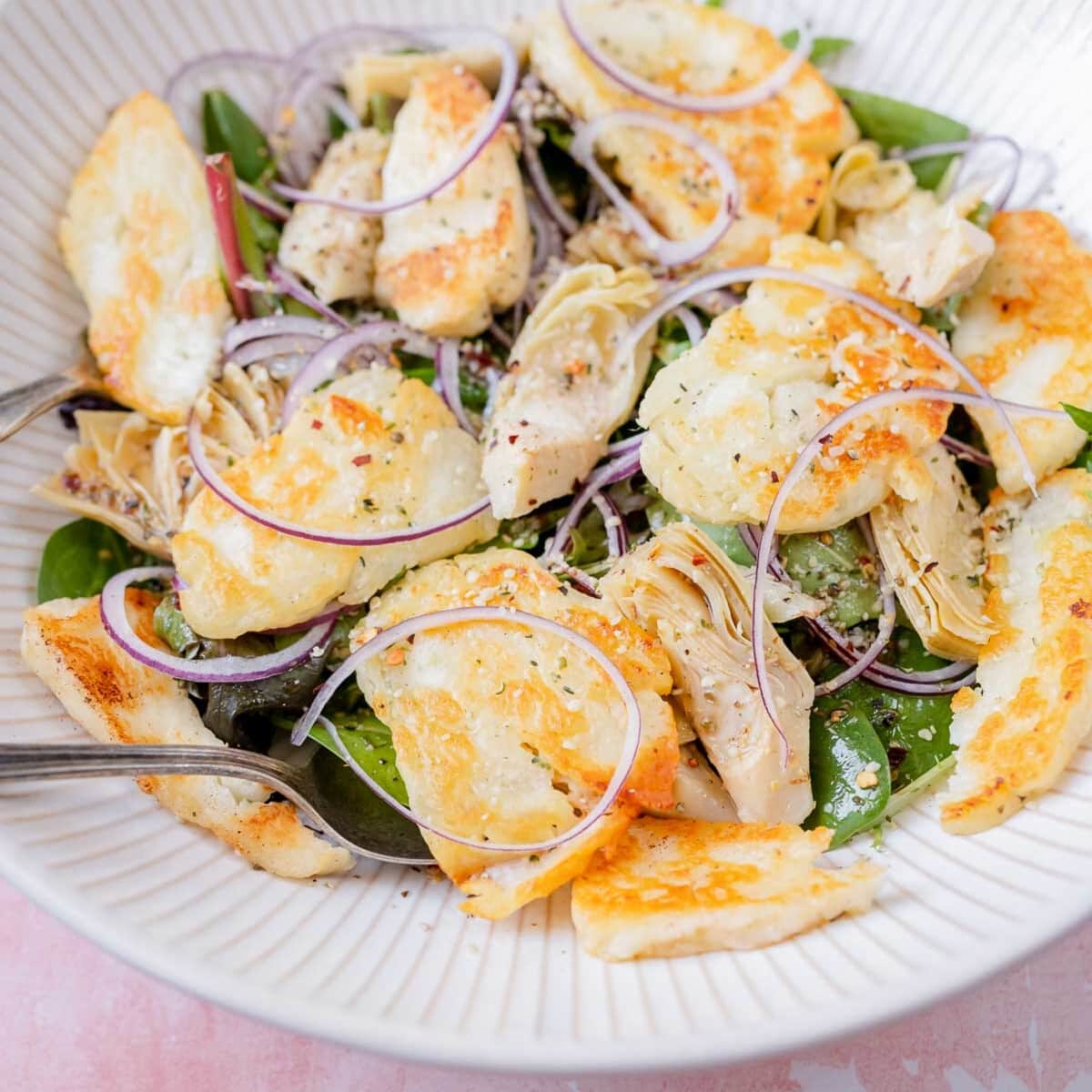 A large white bowl filled with salad greens and golden halloumi cheese slices.