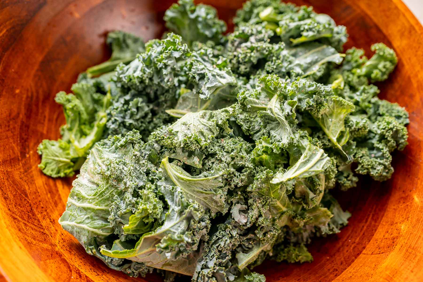 A large wood bowl filled with raw kale leaves.