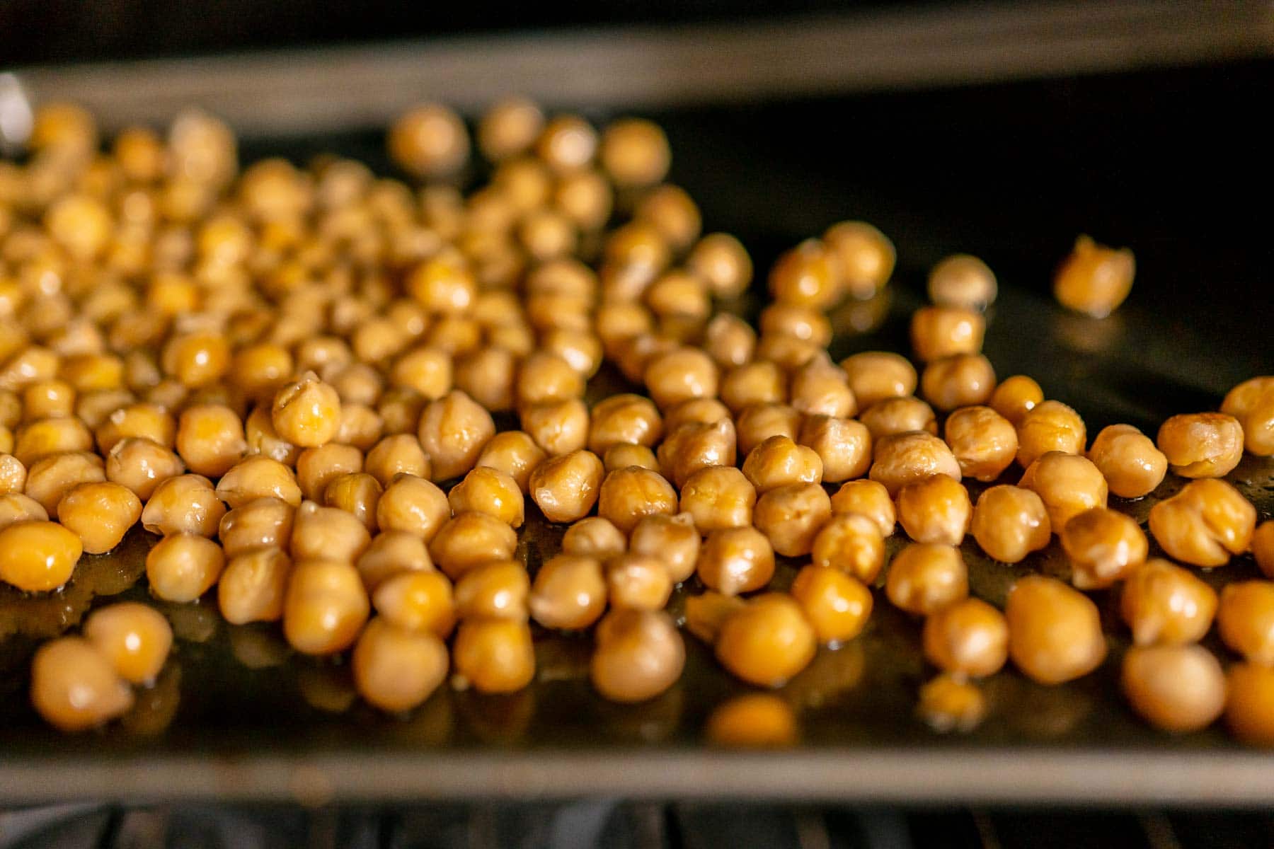 A baking sheet filled with chickpeas on the top rack of the oven.
