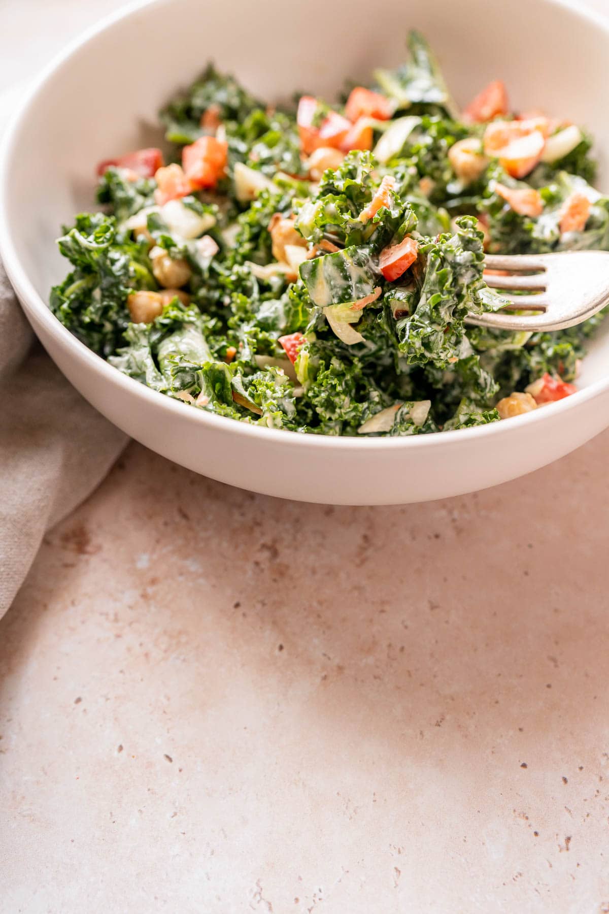 Close shot of a silver fork lifting kale salad out of a white ceramic bowl.