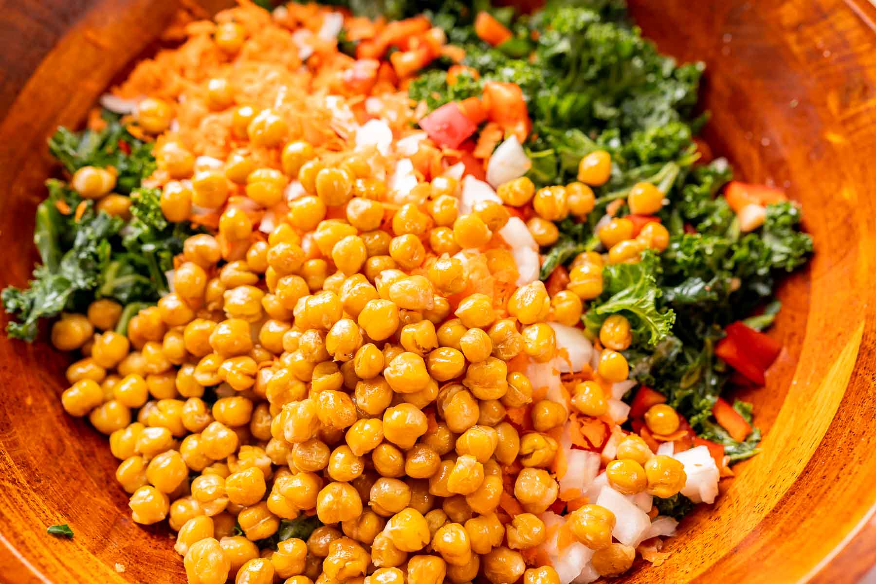 A large wooden bowl filled with kale salad with chickpeas.