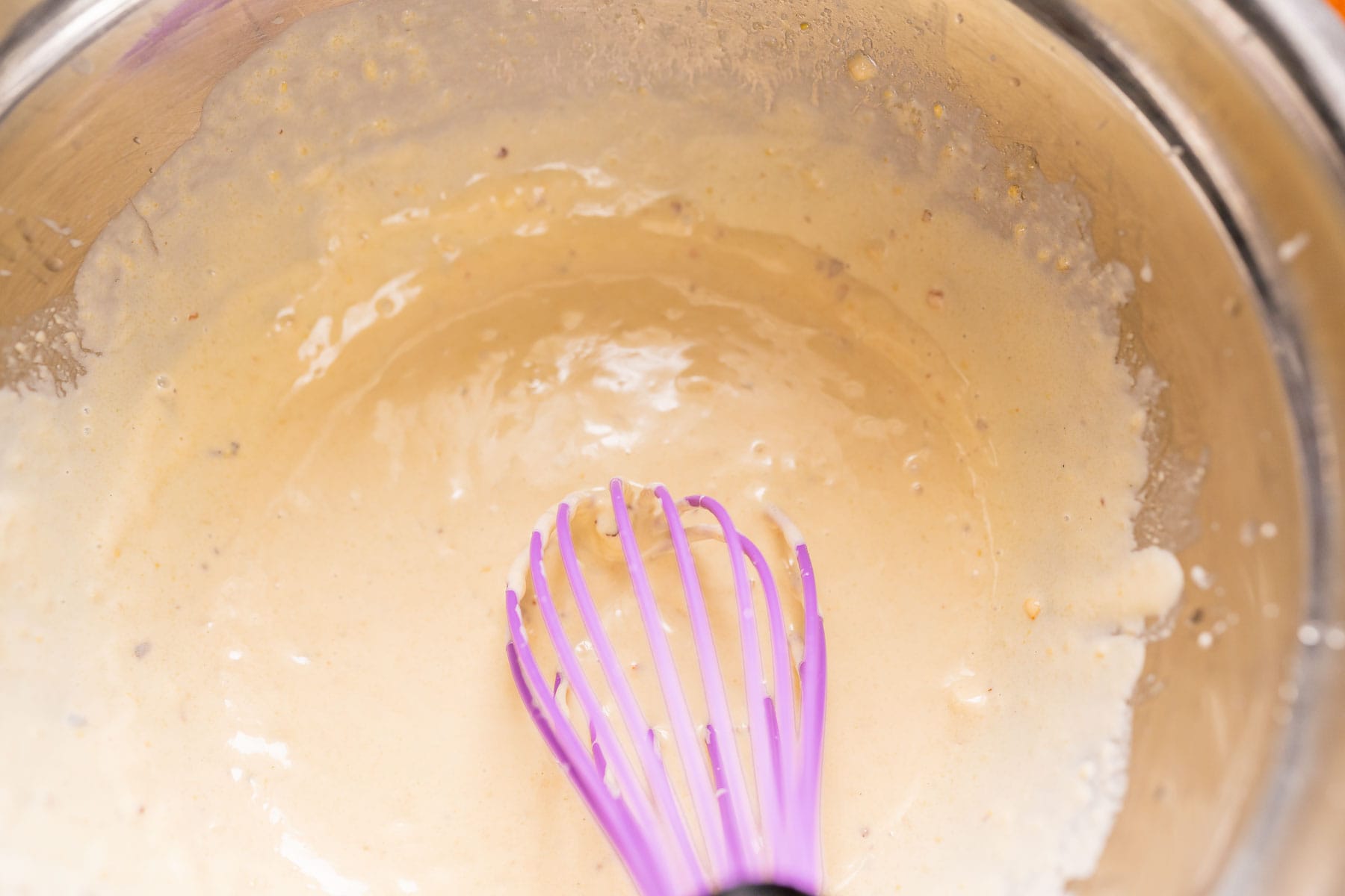 A large silver mixing bowl filled with homemade salad dressing and a purple whisk.