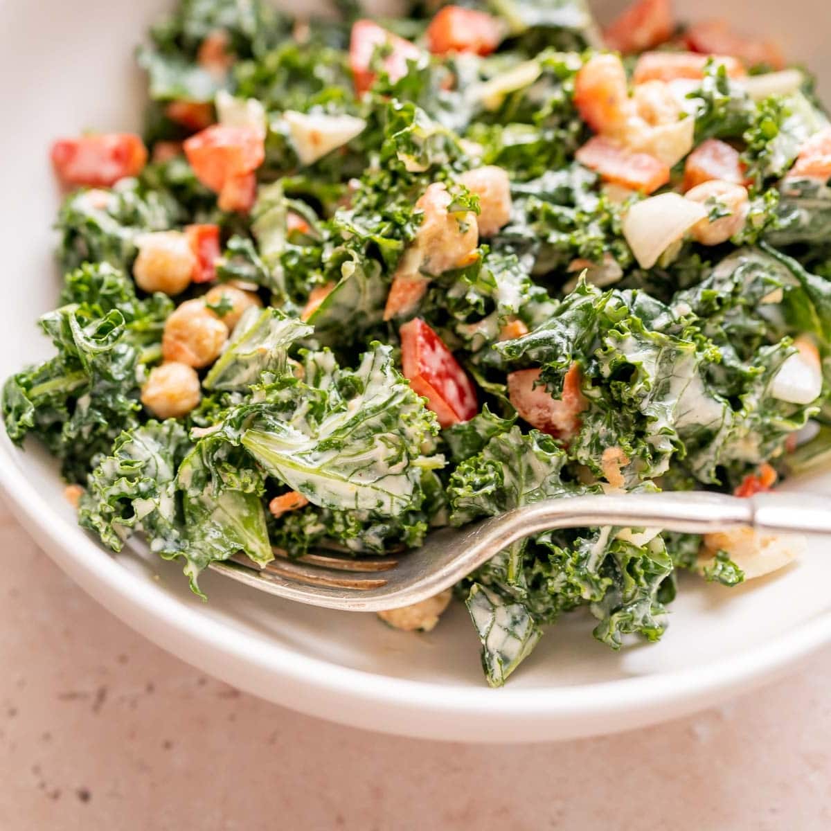 A close shot of a silver fork in a white bowl filled with kale salad.