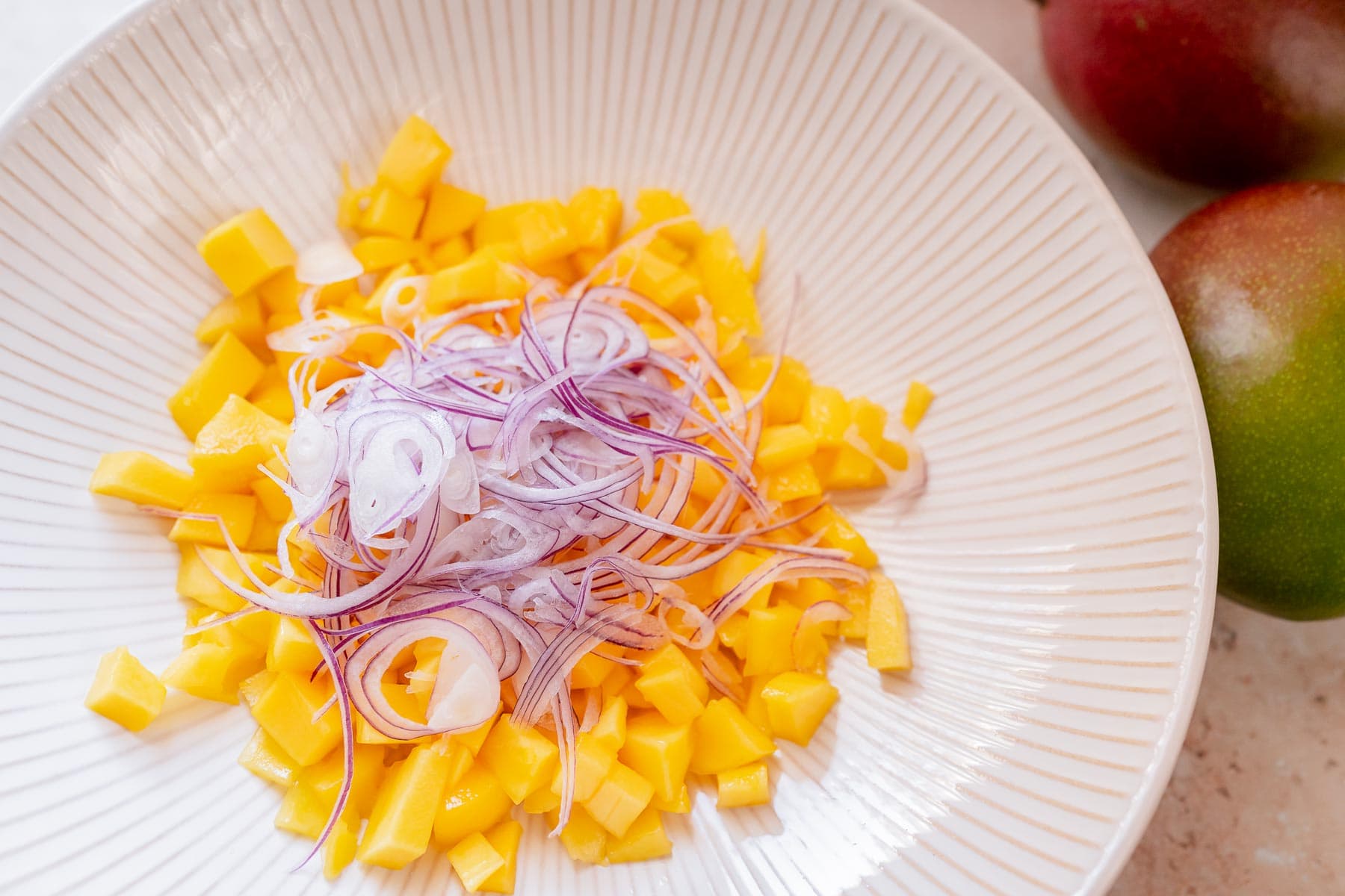 A large bowl filled with diced mango and sliced red onion.