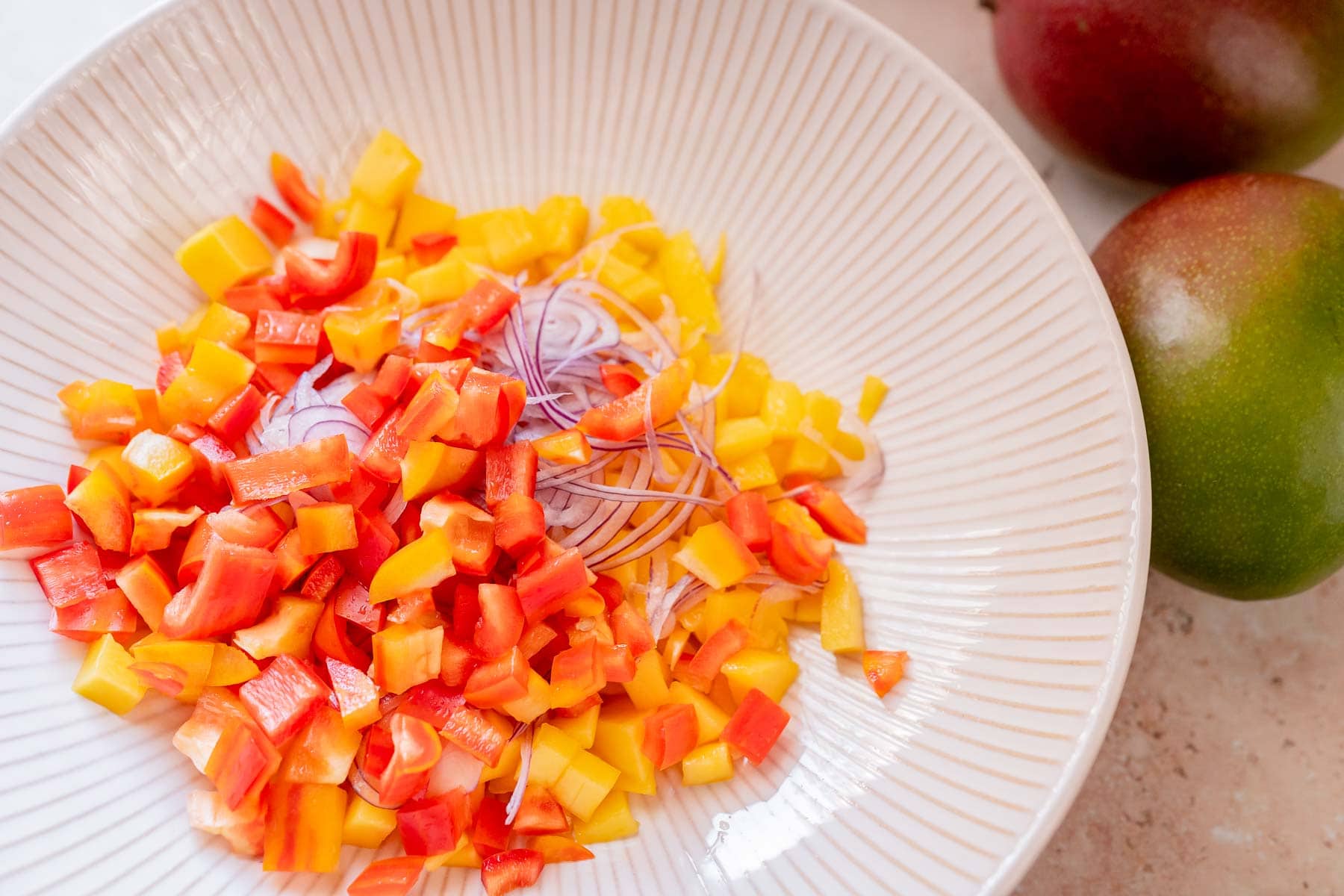 A large white bowl filled with diced mango and bell peppers.