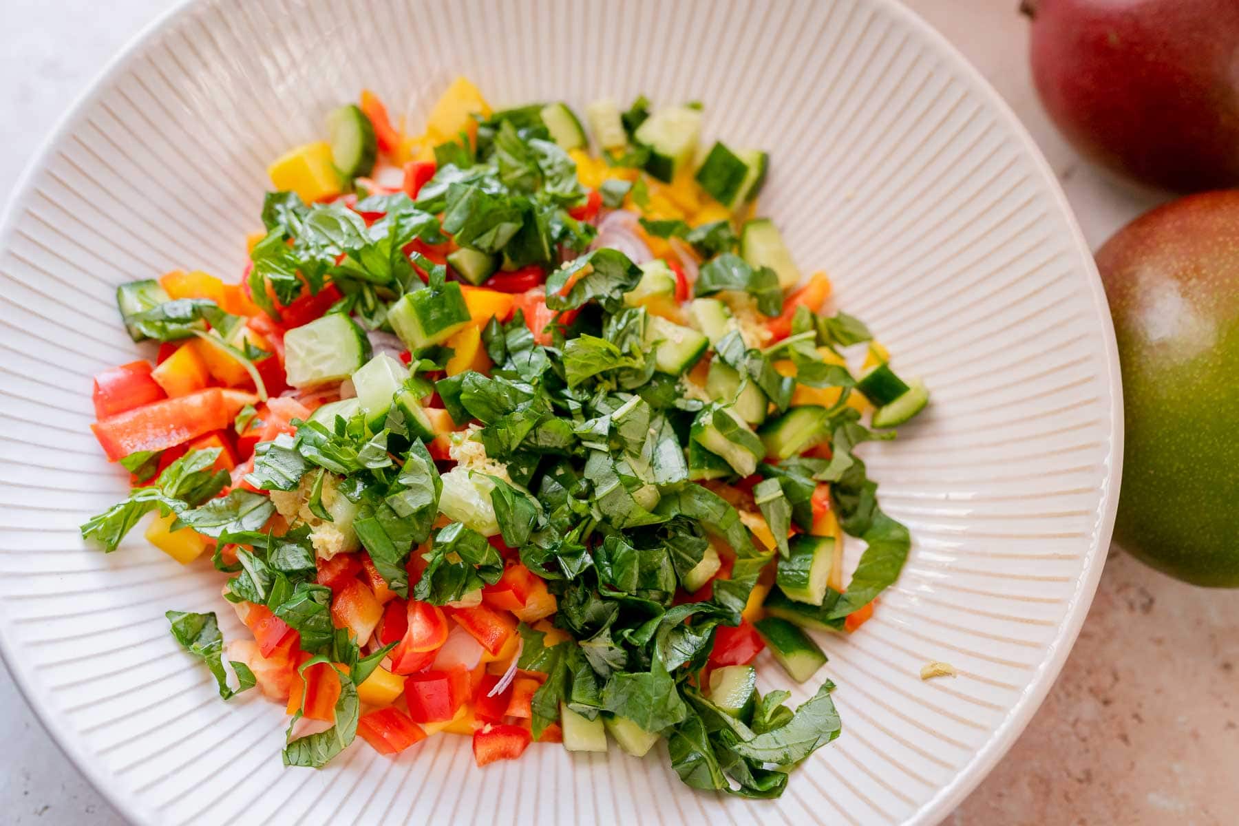 A large white bowl filled with chopped fresh herb, fruit and veggies.