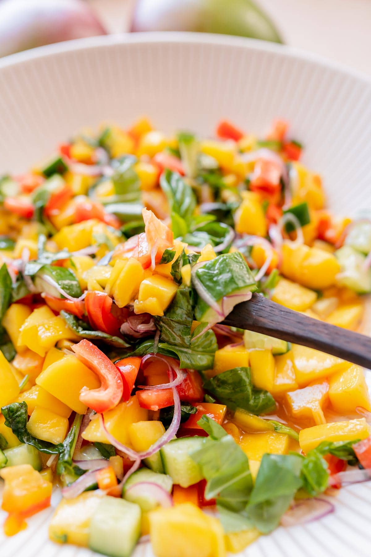 A wooden spoon scooping mango salad out of a bowl.