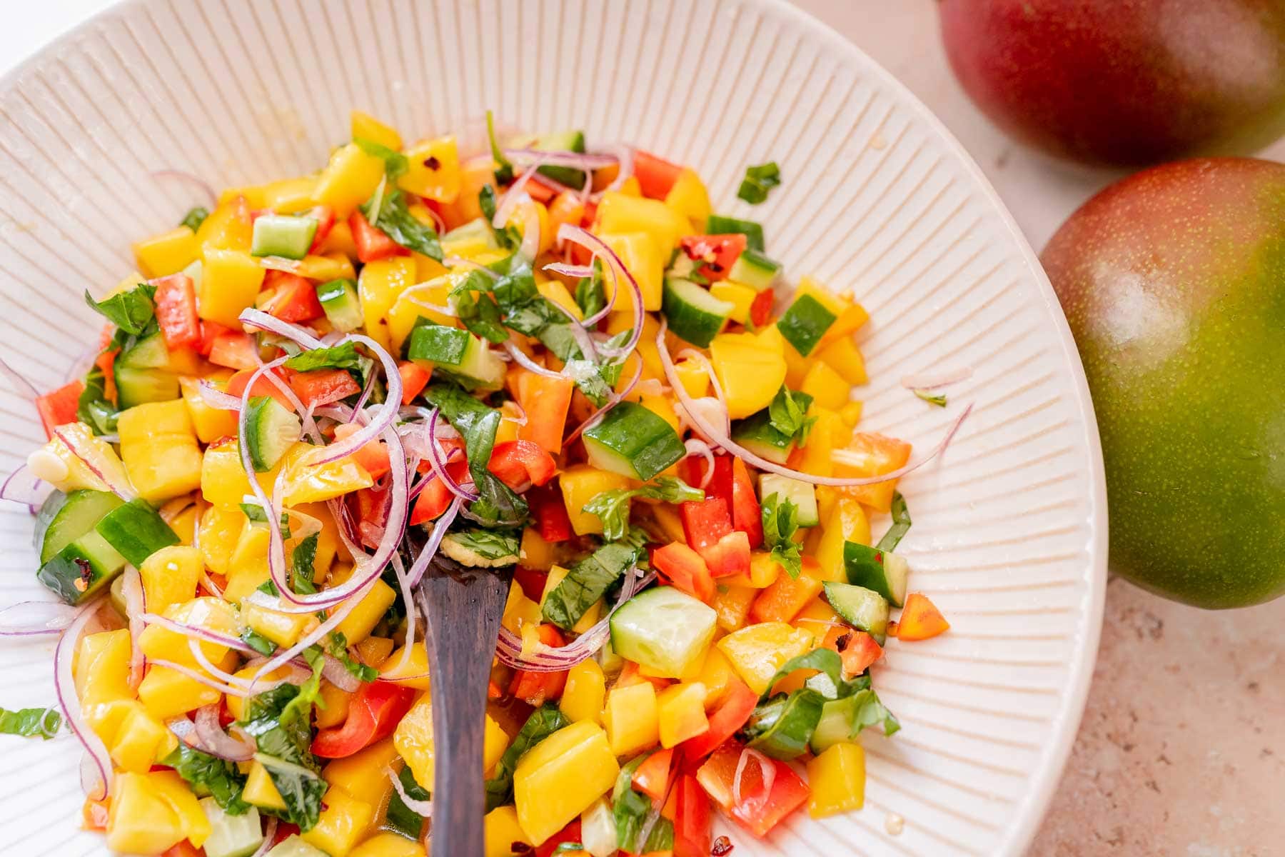 A large white bowl filled with homemade mango salad and a wooden spoon.