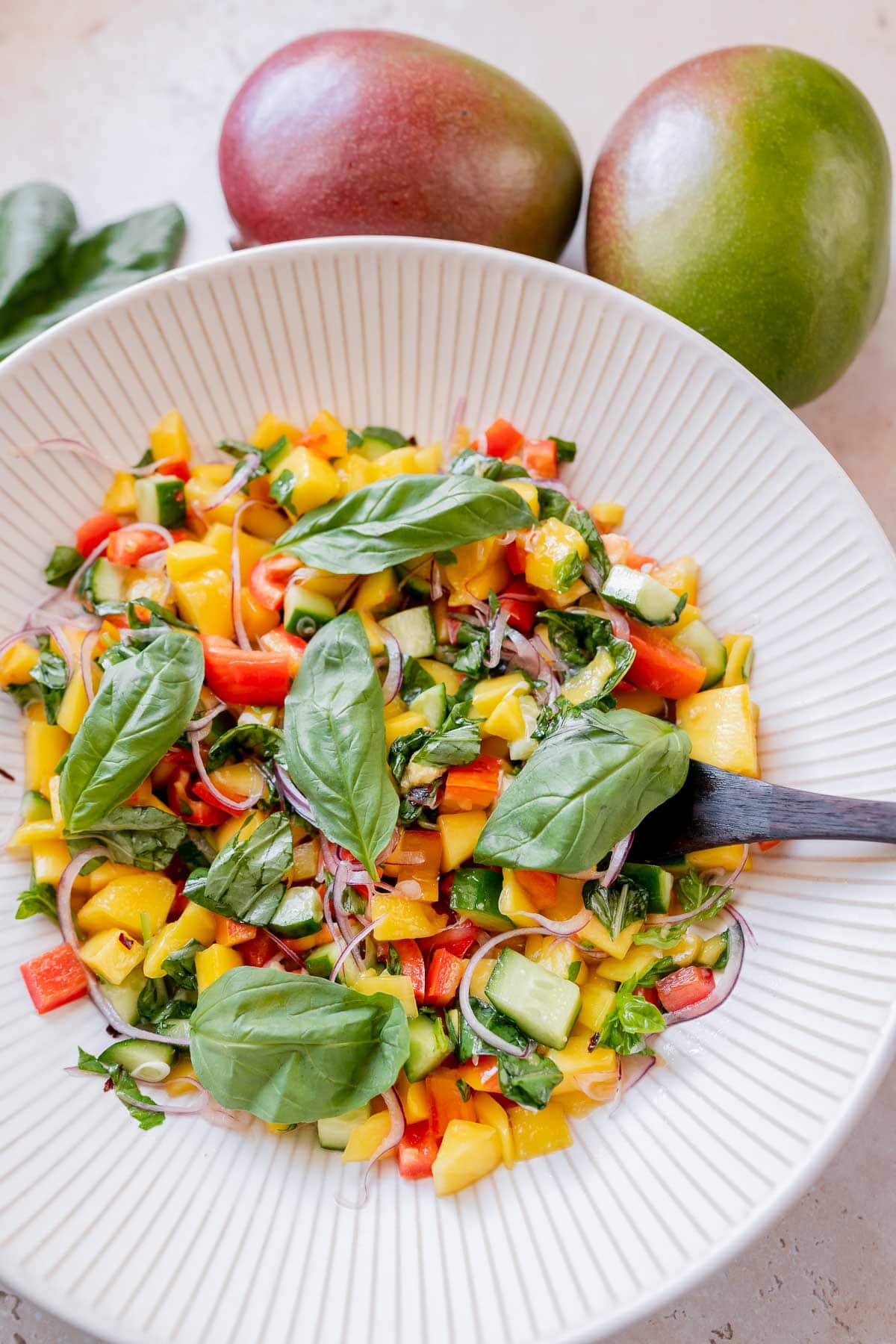 A large white ceramic bowl filled with mango, fresh herbs, and veggies.