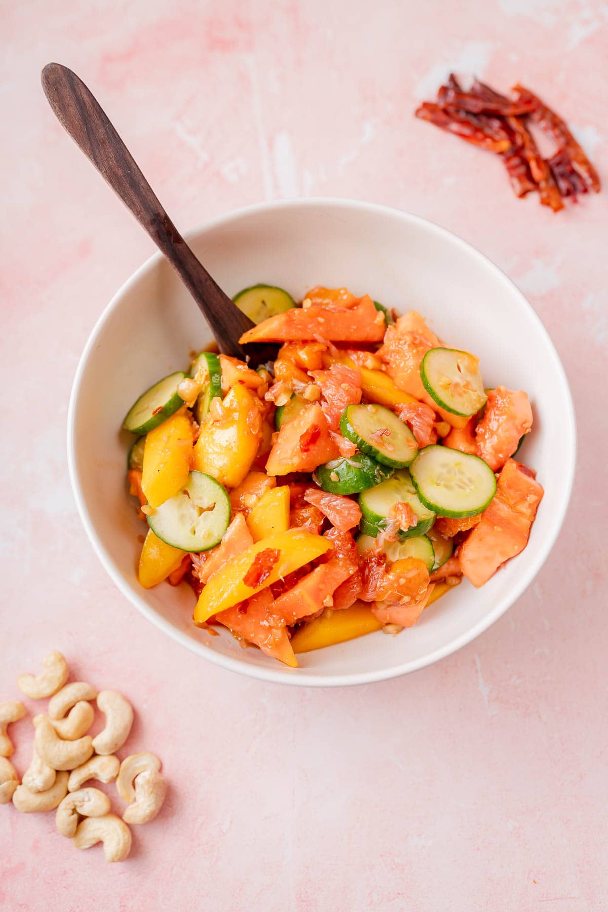 A white bowl of tropical fruit salad coated in a spicy looking dressing.