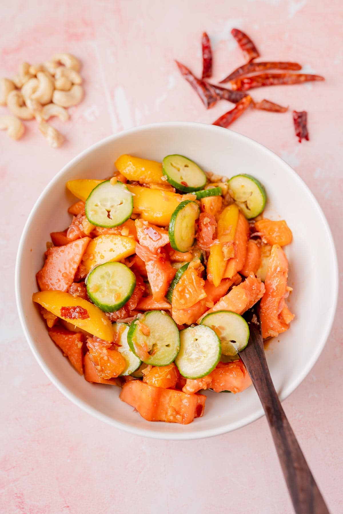 A white bowl filled with a variety of sliced fruit and a wooden spoon.