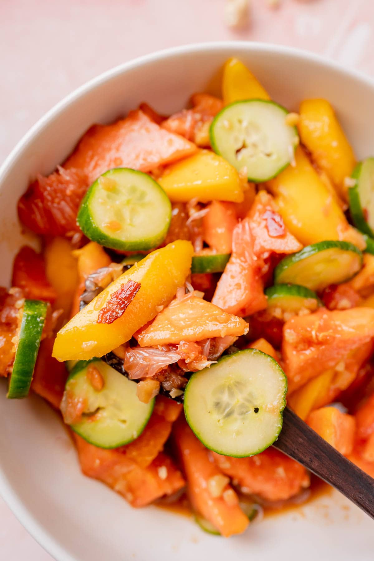 Close shot of a spoonful of fruit salad resting in a white bowl.