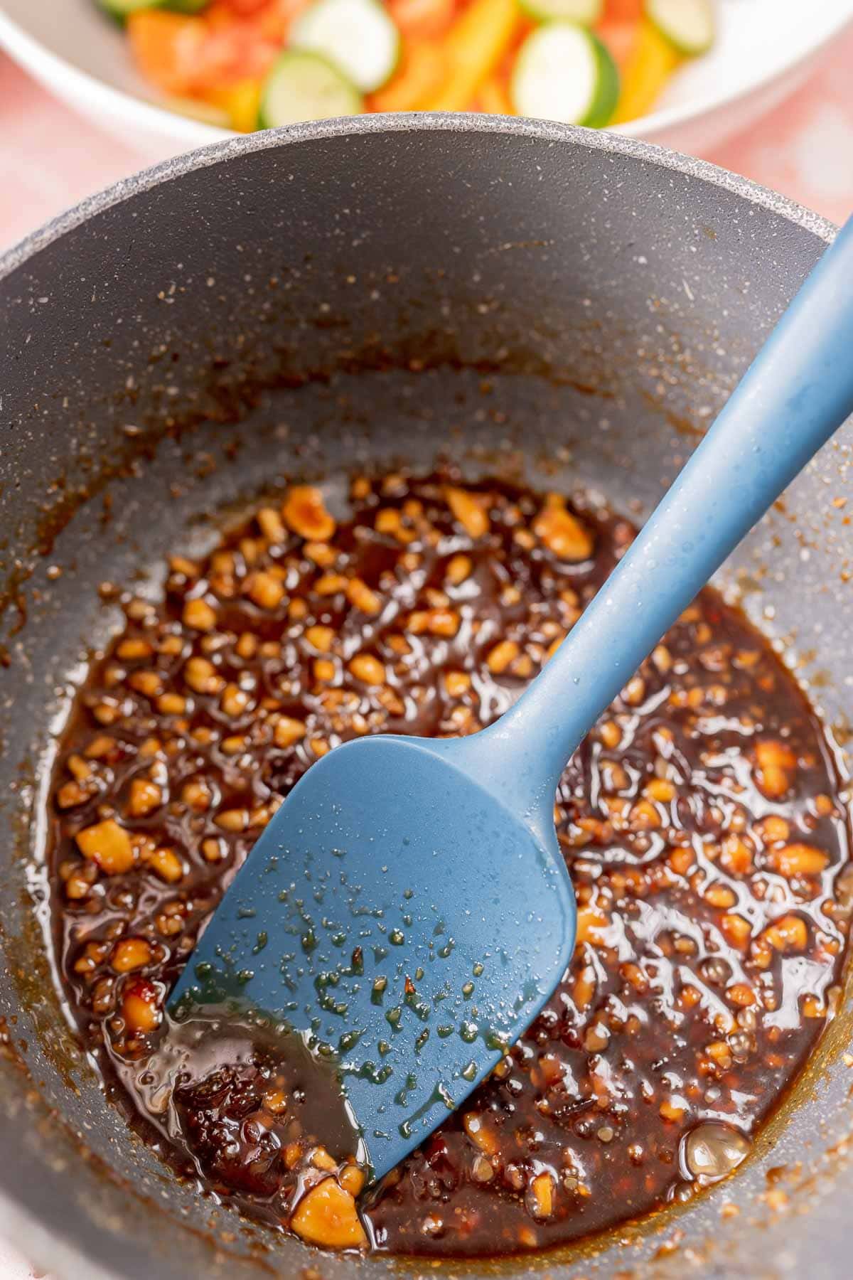 A saucepan filled with a sticky looking liquid and a blue spatula.