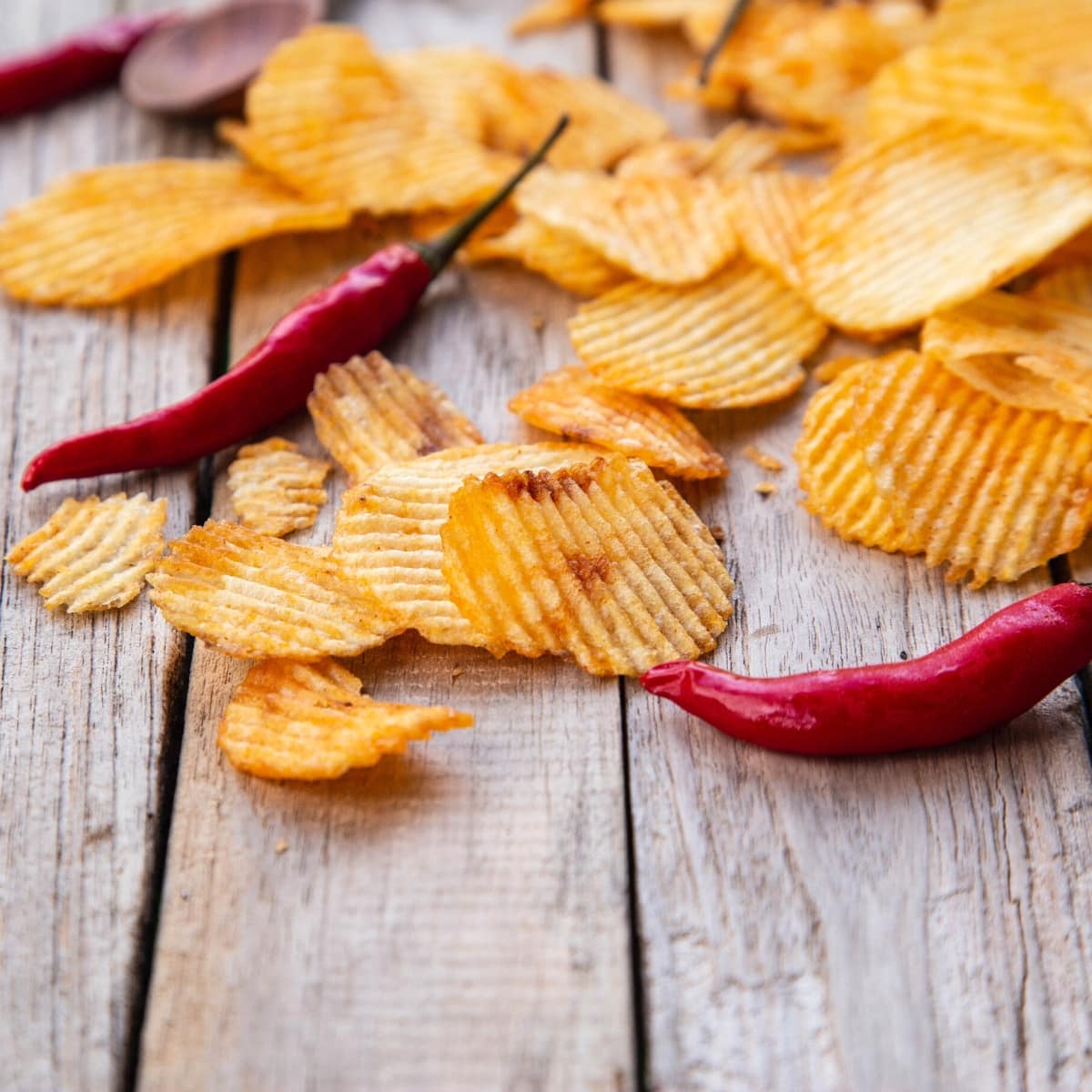 Potato chips and red chiles resting on a wooden table.