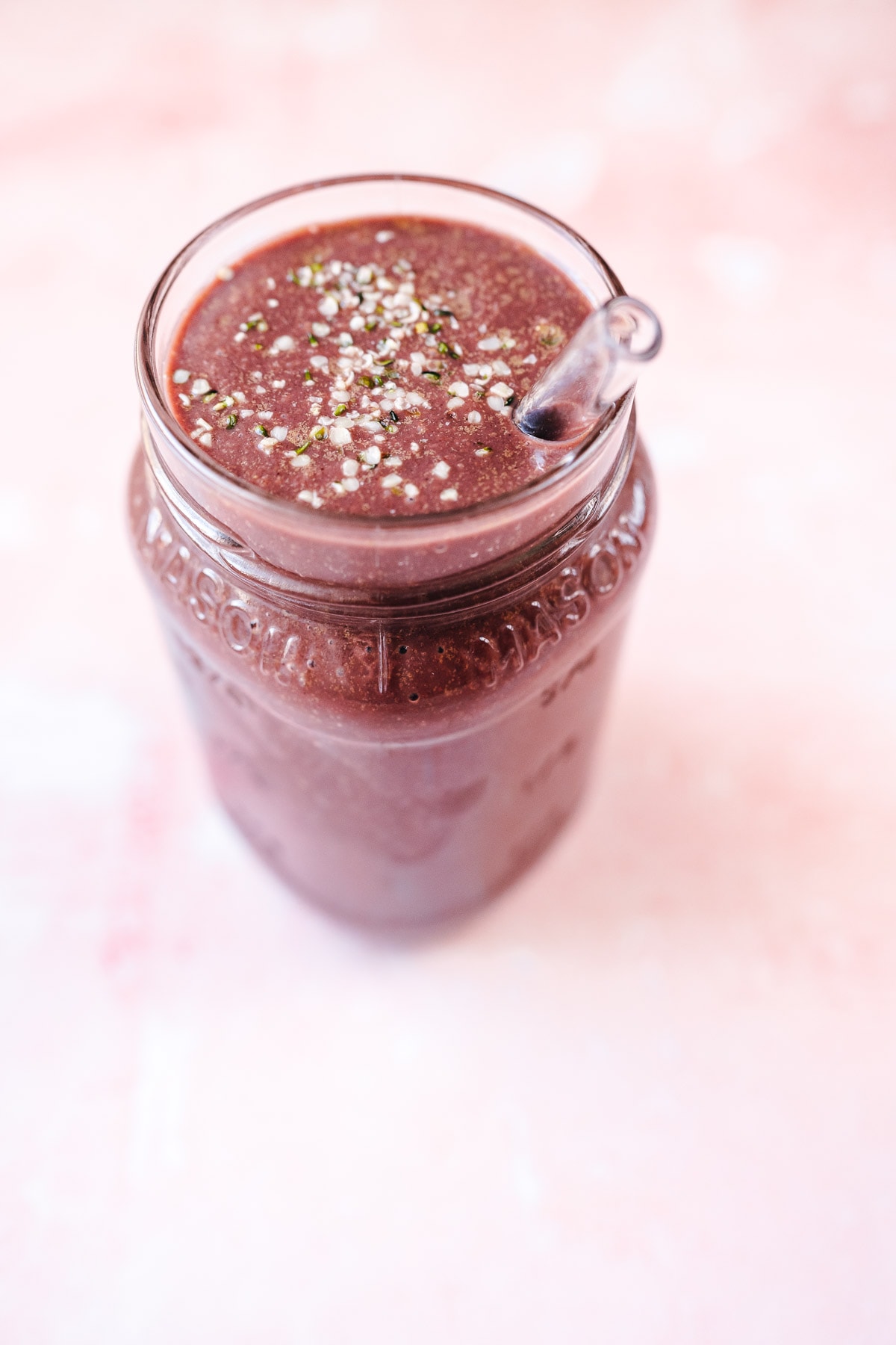 Close shot of a purple smoothie in a glass jar sprinkled with white seeds.