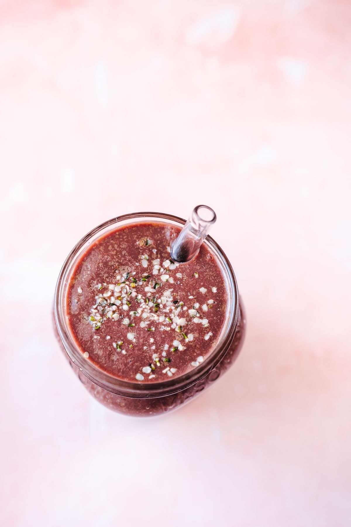 Top view of a purple smoothie sprinkled with seeds in a glass jar with a glass straw.