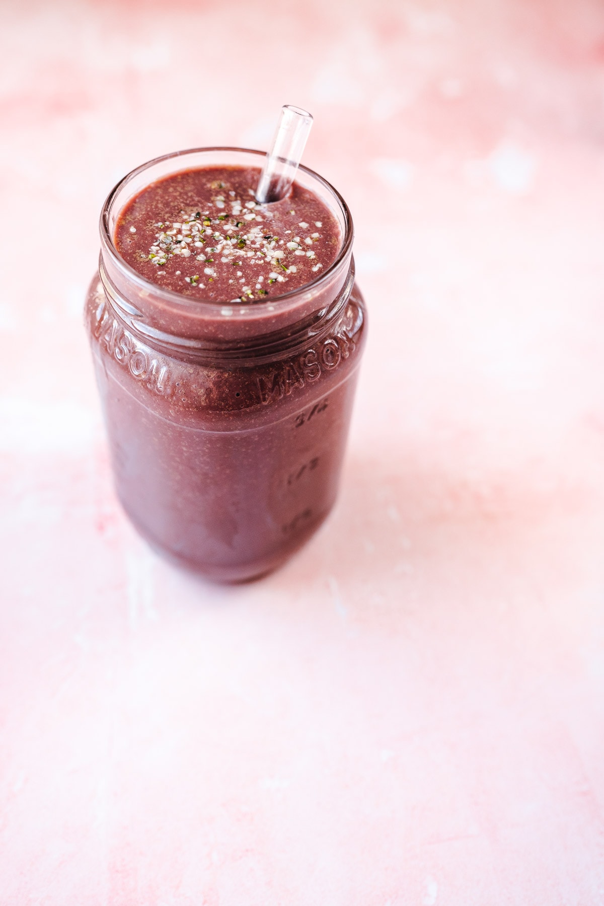 A glass mason jar filled with a dark purple smoothie with a glass straw.