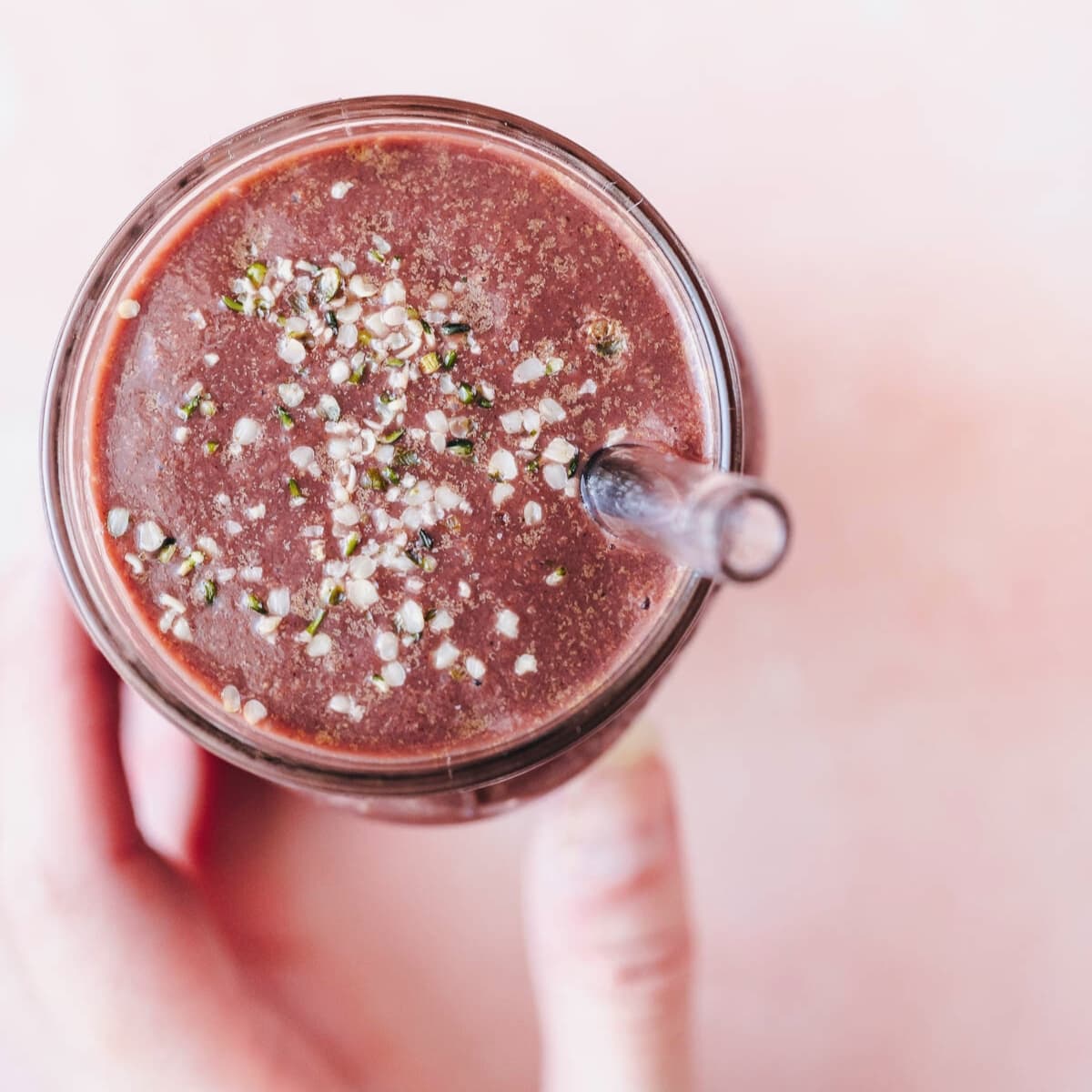 A hand holds a dark purple smoothie smoothie in a glass jar.