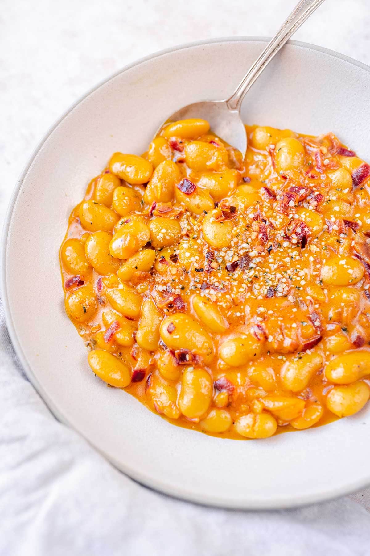 A silver spoon resting in a large ceramic bowl filled with vibrant yellow cooked beans.