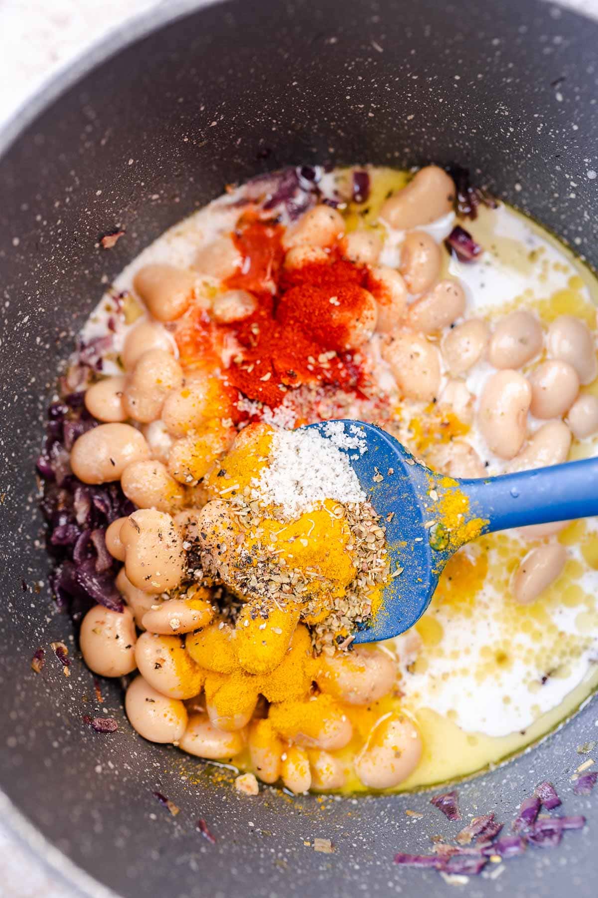 Spices resting atop of pot of butter beans, coconut milk and onions.