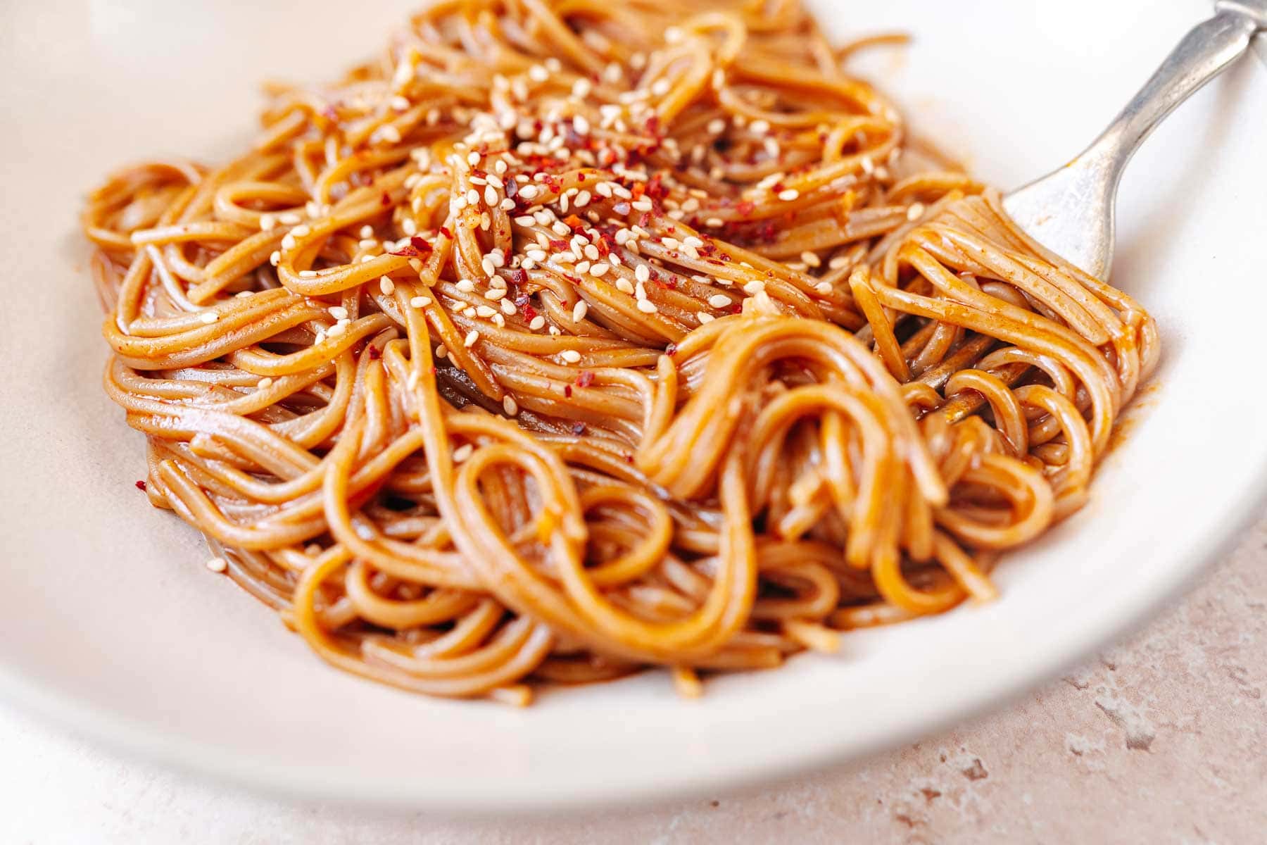 Red noodles in a ceramic bowl topped with seeds.