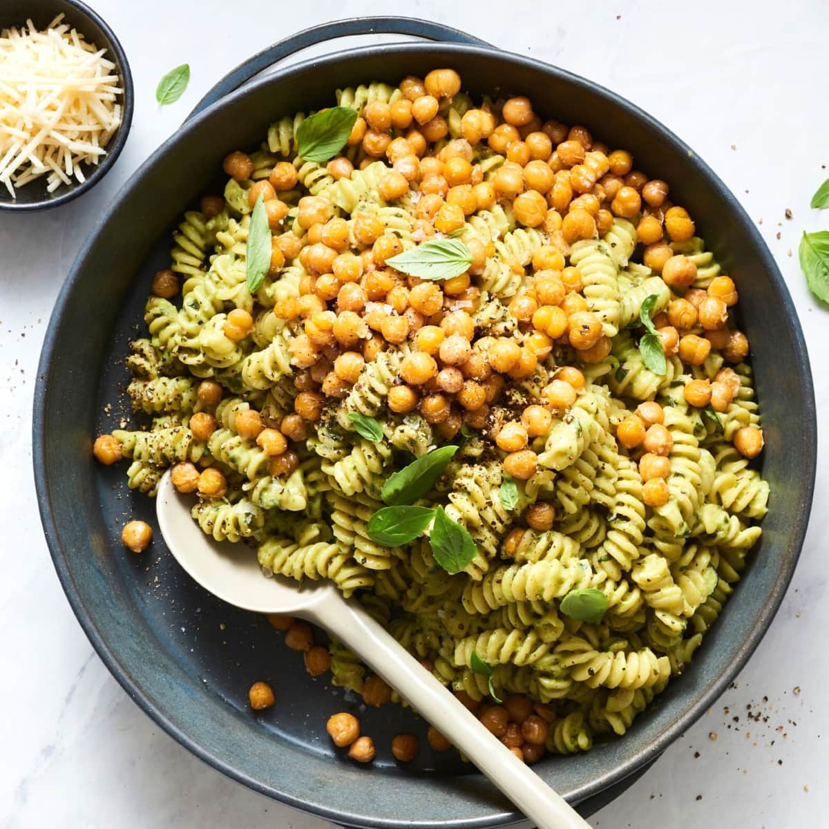 A black skillet filled with green pasta and chickpeas.
