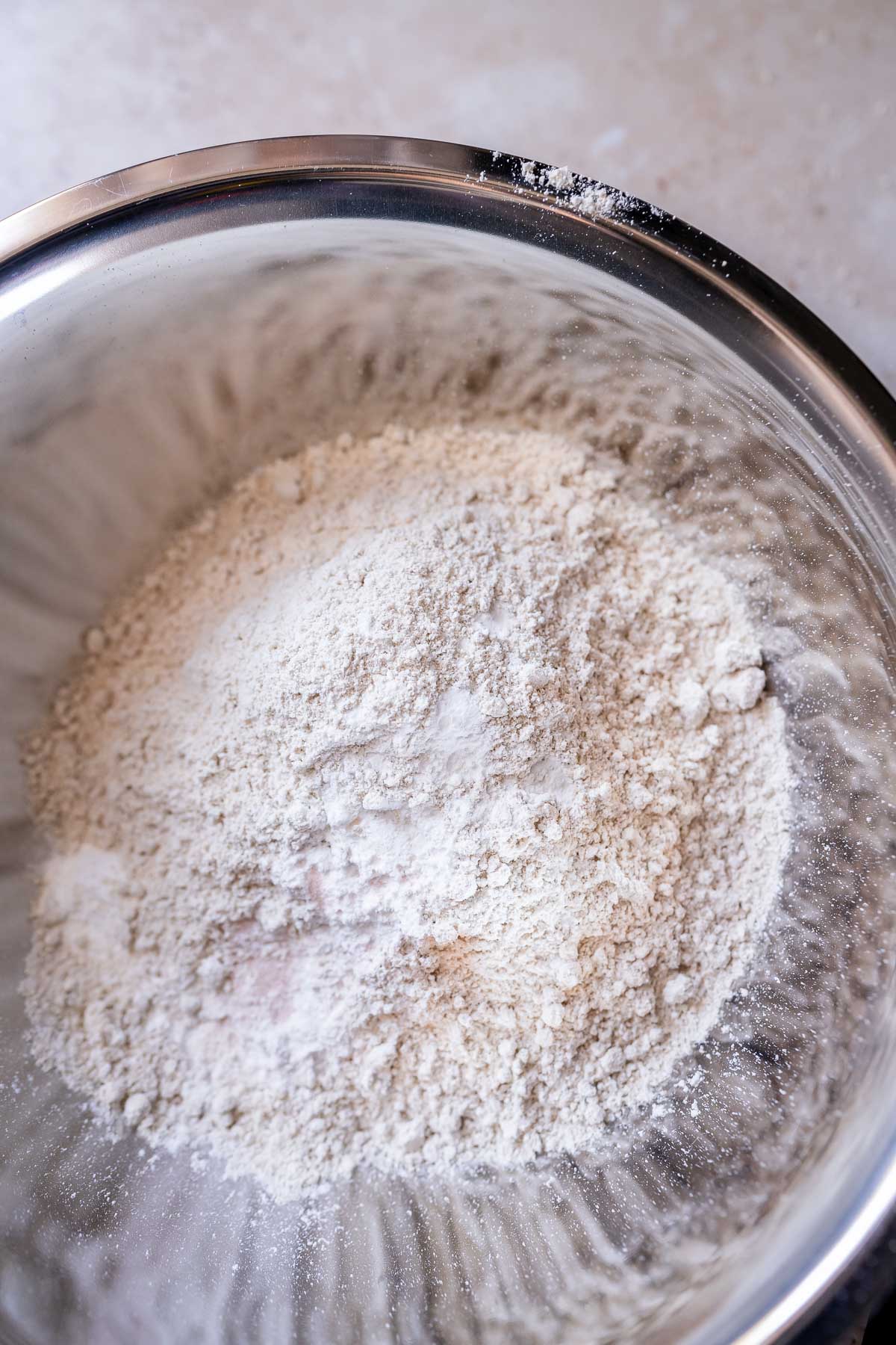 A silver mixing bowl filled with white flour and other dry ingredients.