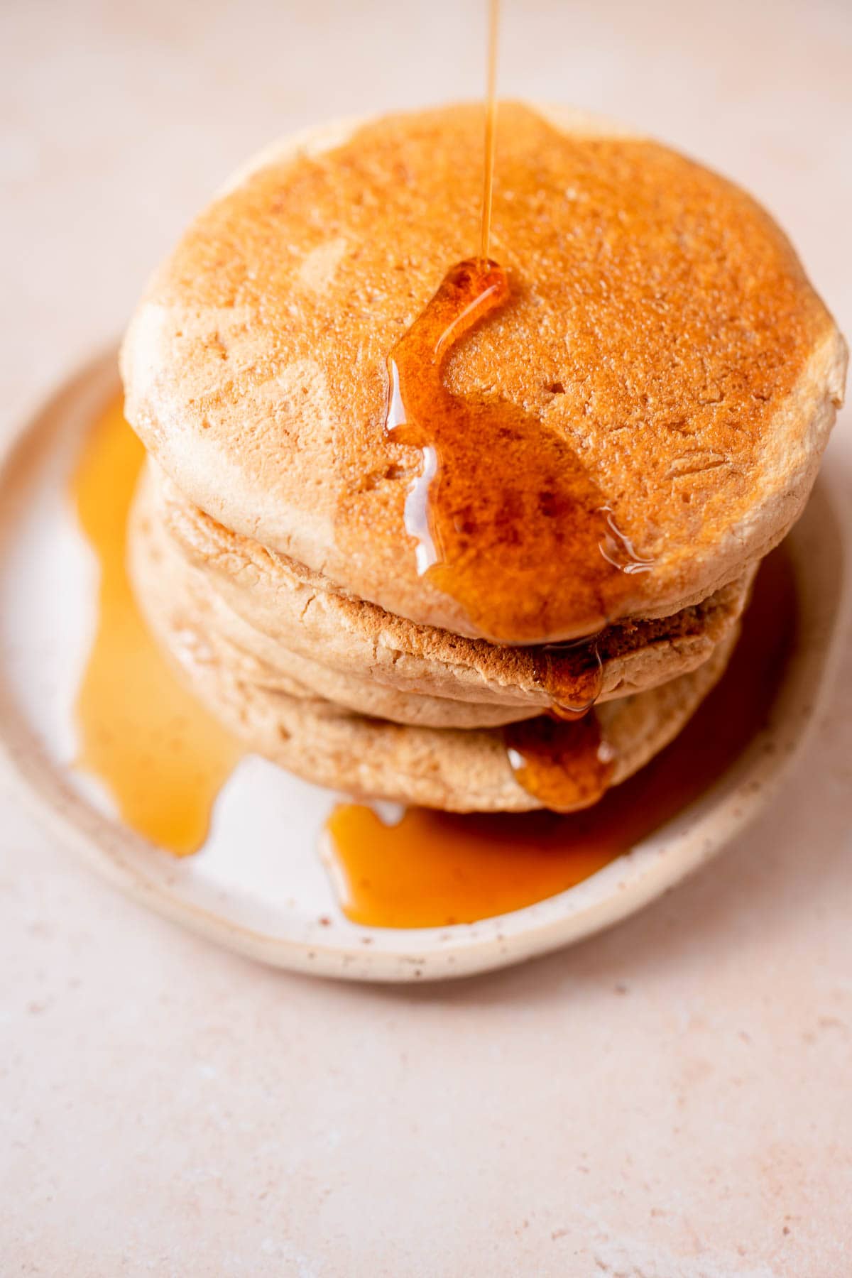 A stack of pancakes being drizzled with maple syrup.
