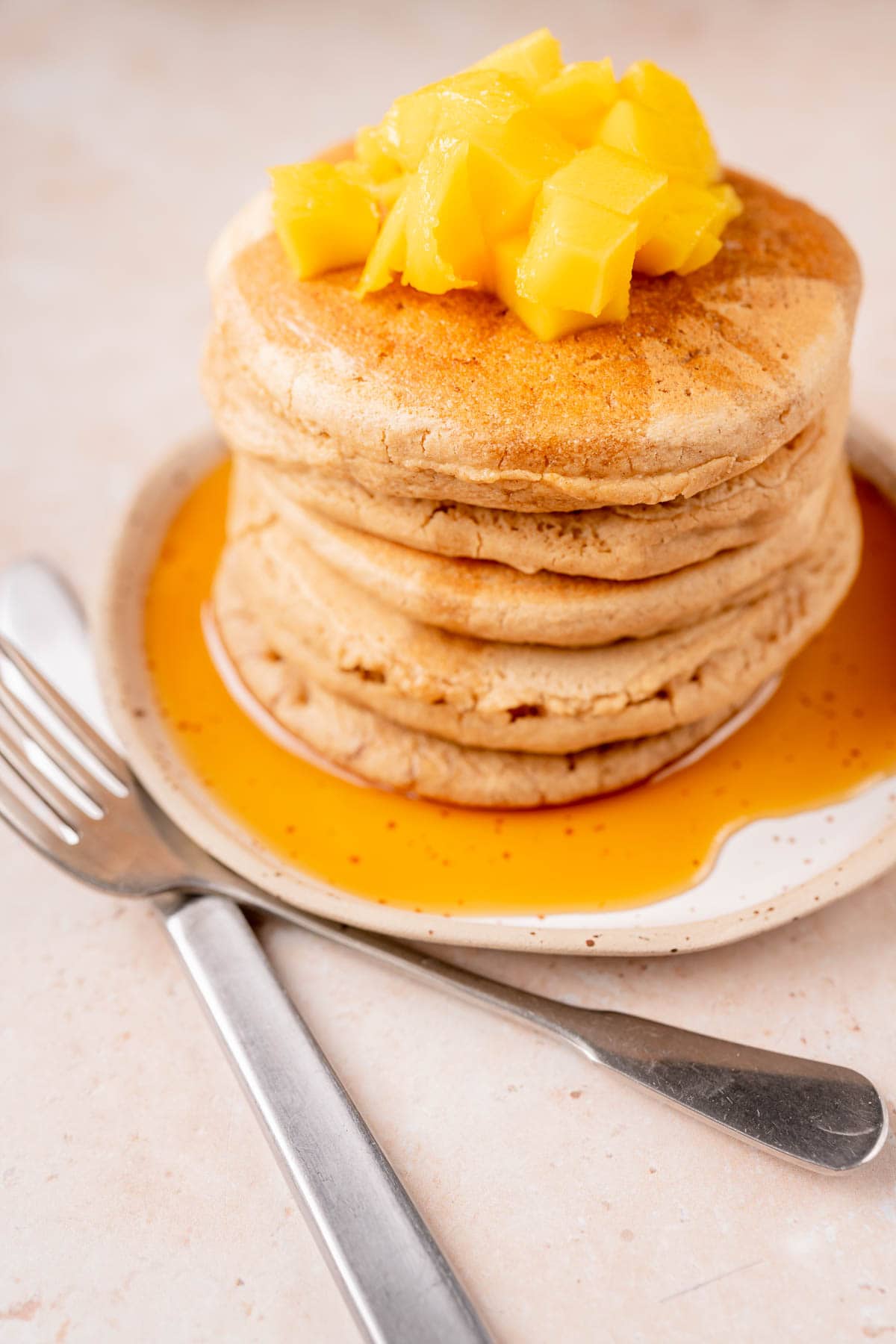 A stack of oat flour pancakes topped with syrup and mango.