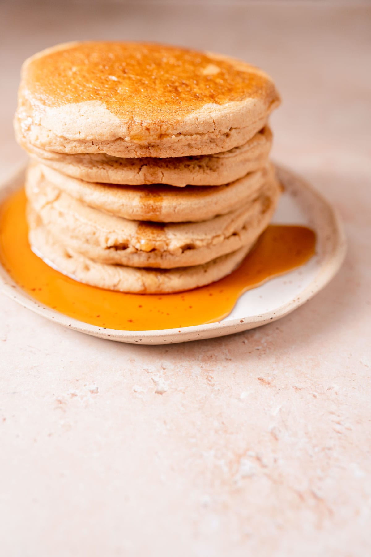 A stack of pancakes drizzled with maple syrup resting a ceramic plate.