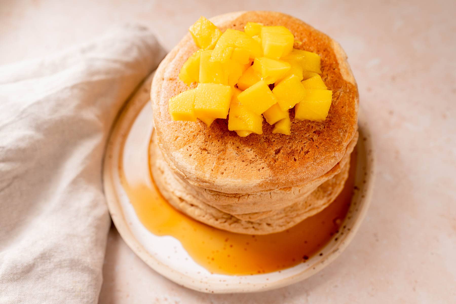 A plate with a stack of pancakes topped with chopped mango and maple syrup.