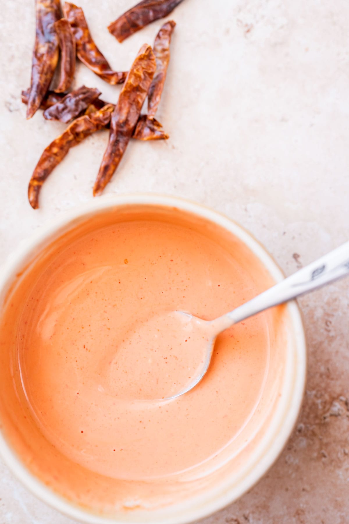 A spoon rests in a small ceramic dish of spicy mayo.