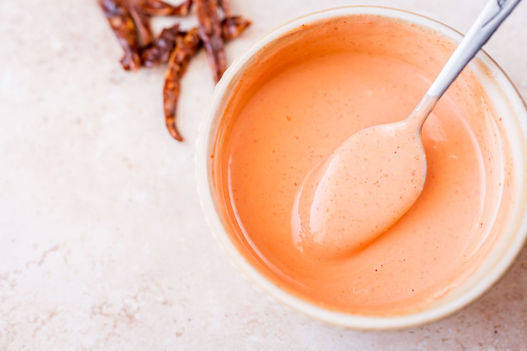 A silver spoon rests in a small bowl of spicy aioli.