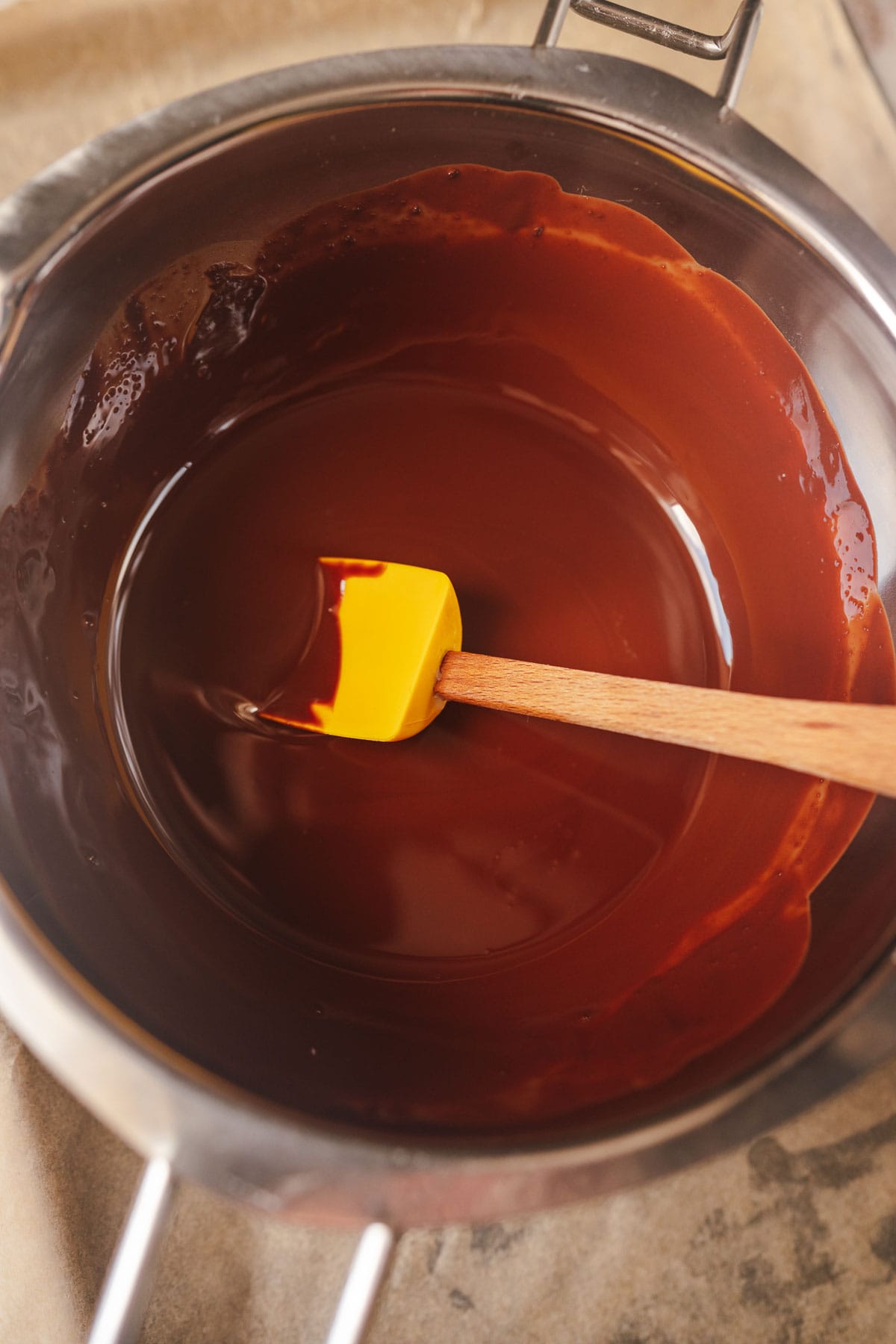 A silver double boiler filled with melted chocolate and a yellow spatula.
