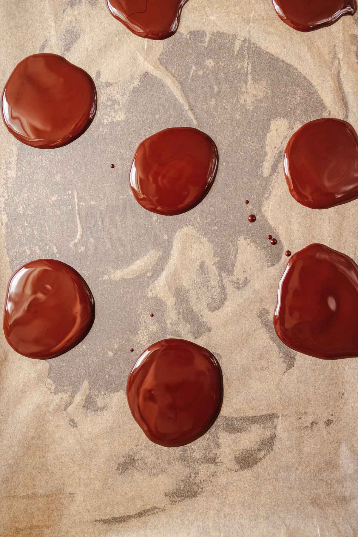 Small puddles of melted chocolate on tan parchment paper.