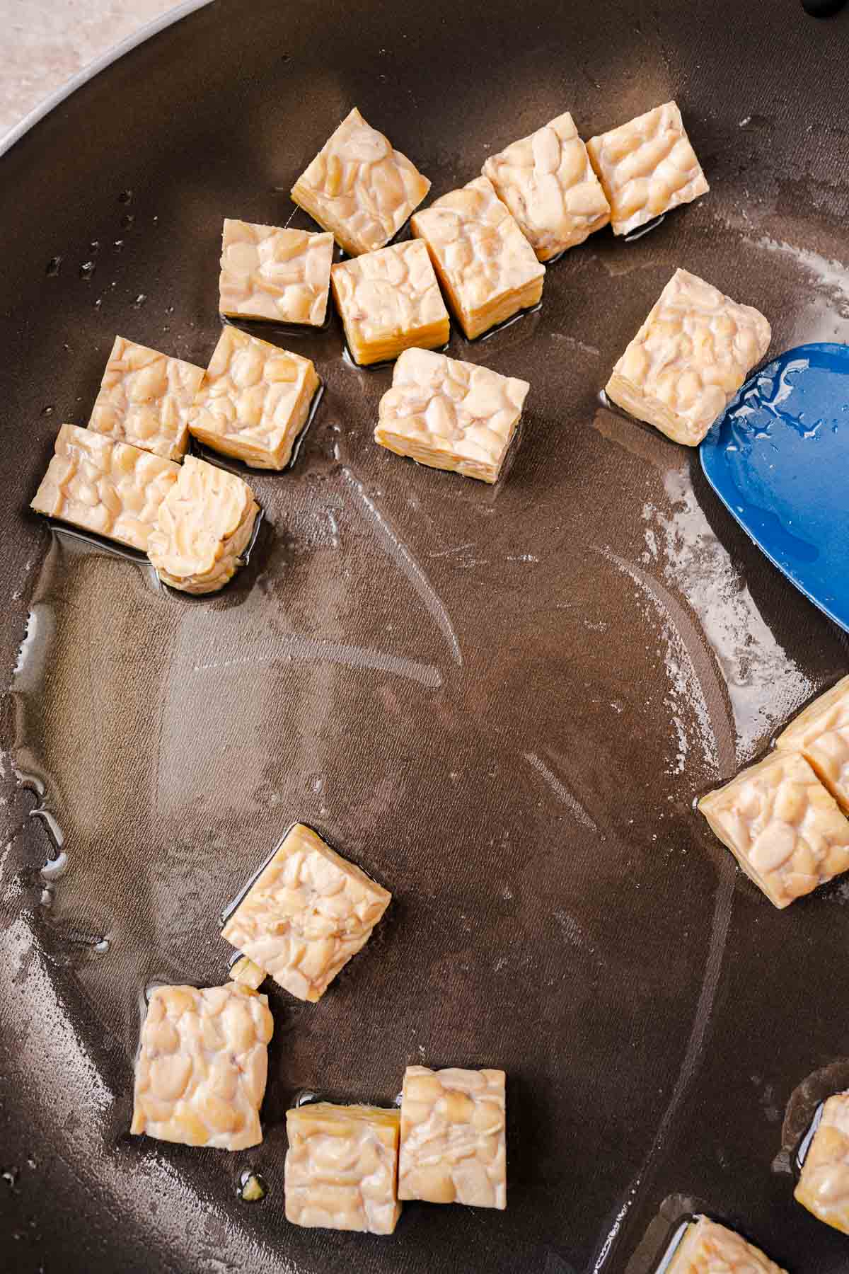 A skillet with oil and uncooked tempeh.