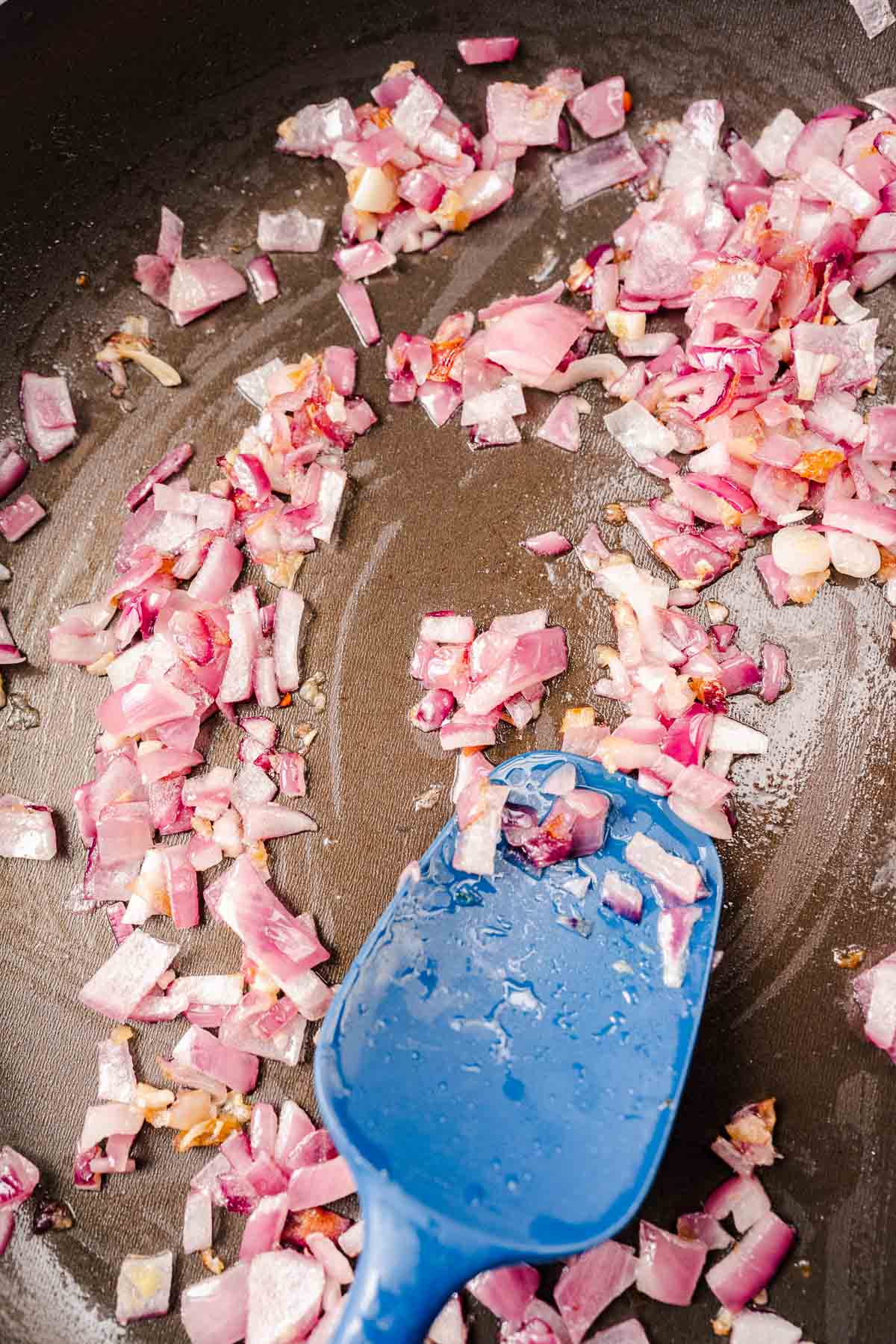 An oiled skillet with chopped red onions.