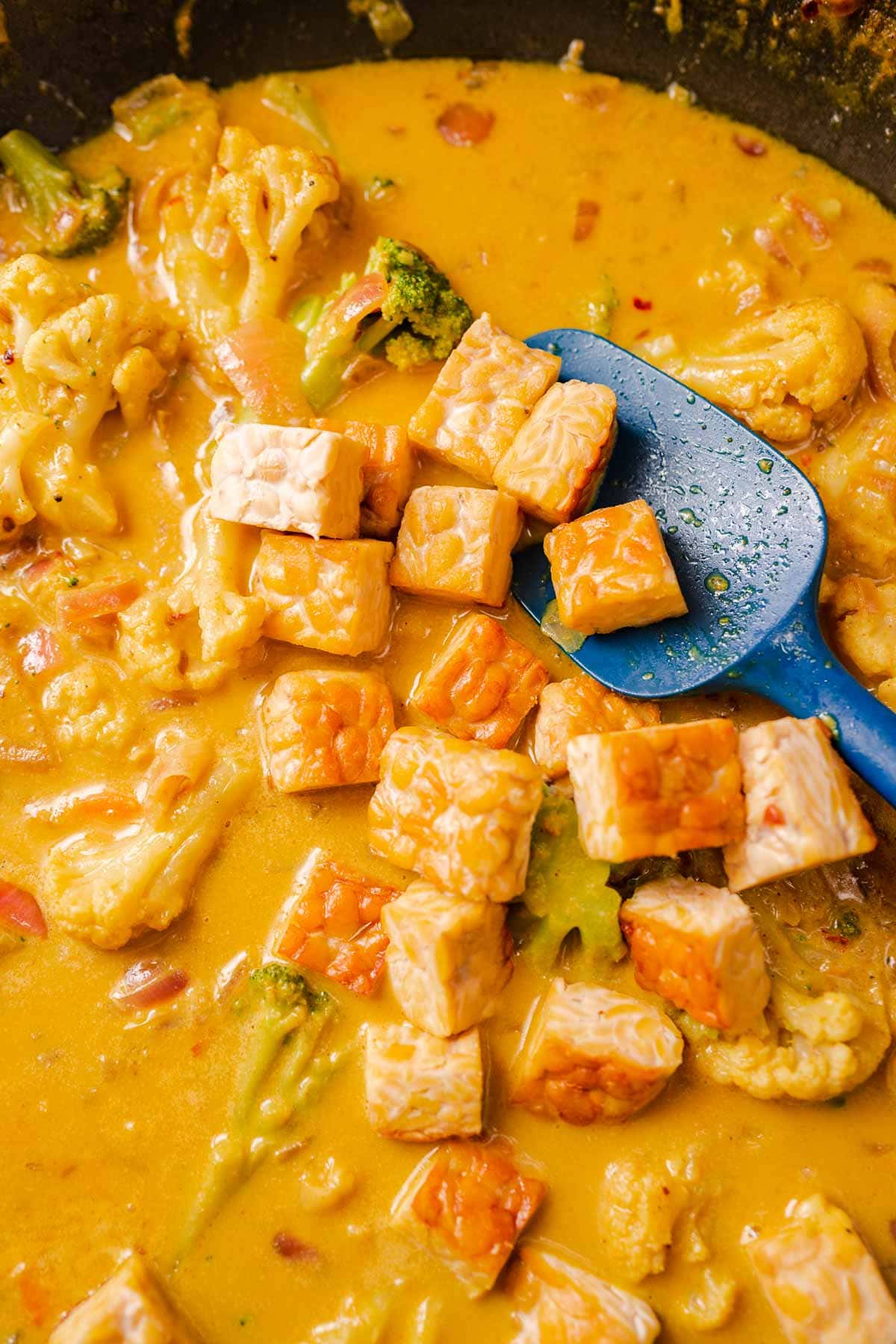 Close shot of cubed tempeh in a yellow curry broth.