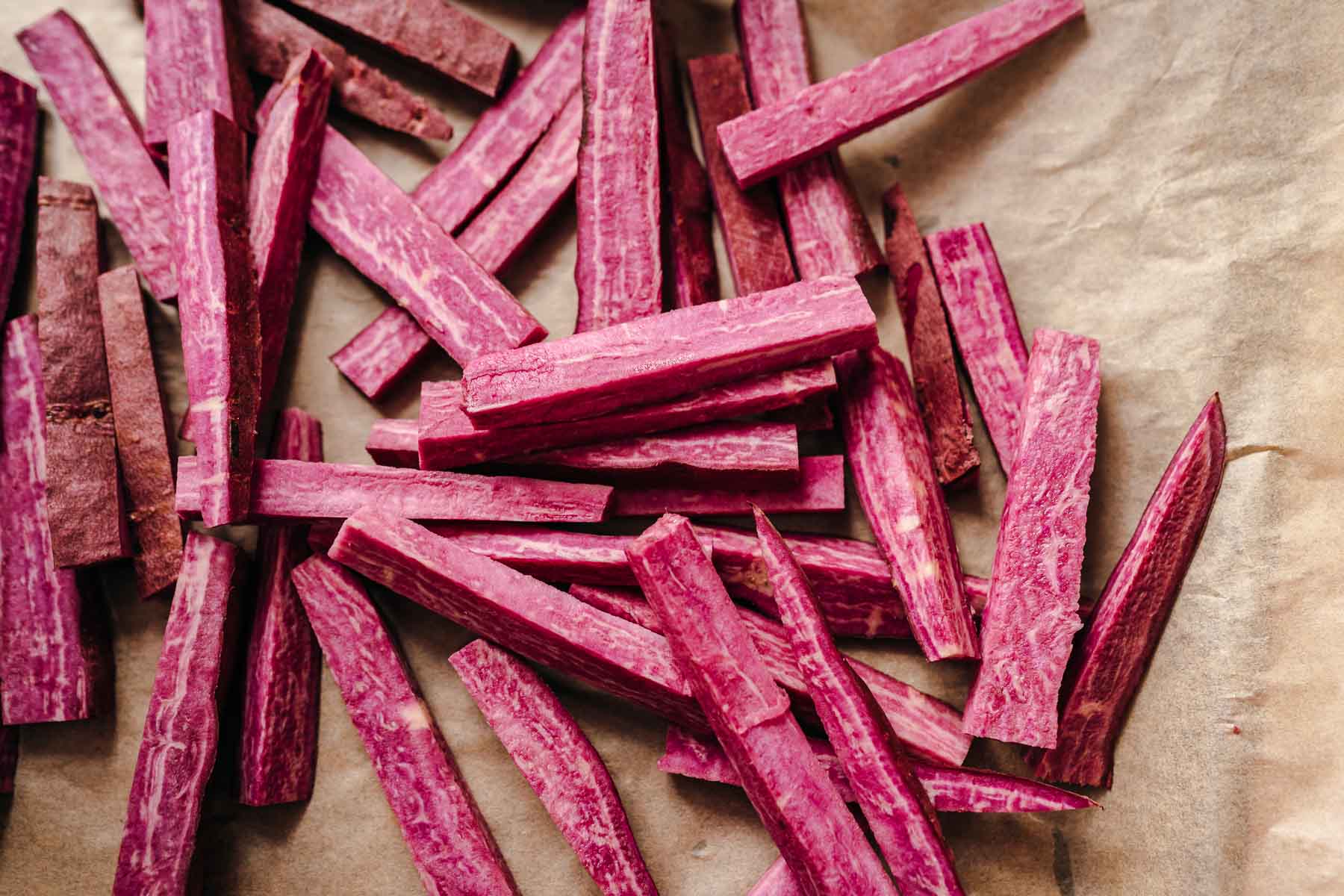 Uncooked cut purple fries on parchment paper.