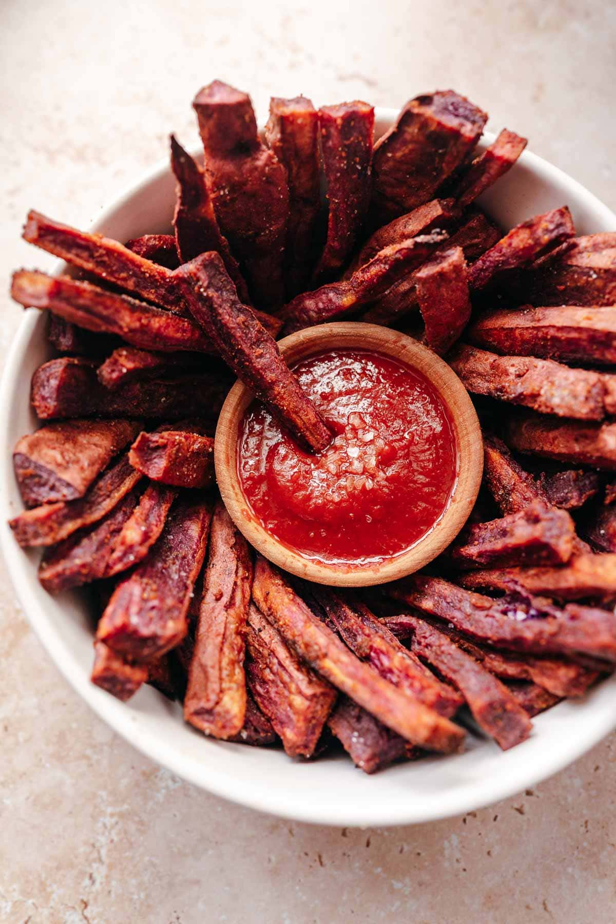 A white bowl filled with purple cooked fries and a small bowl of red ketchup.