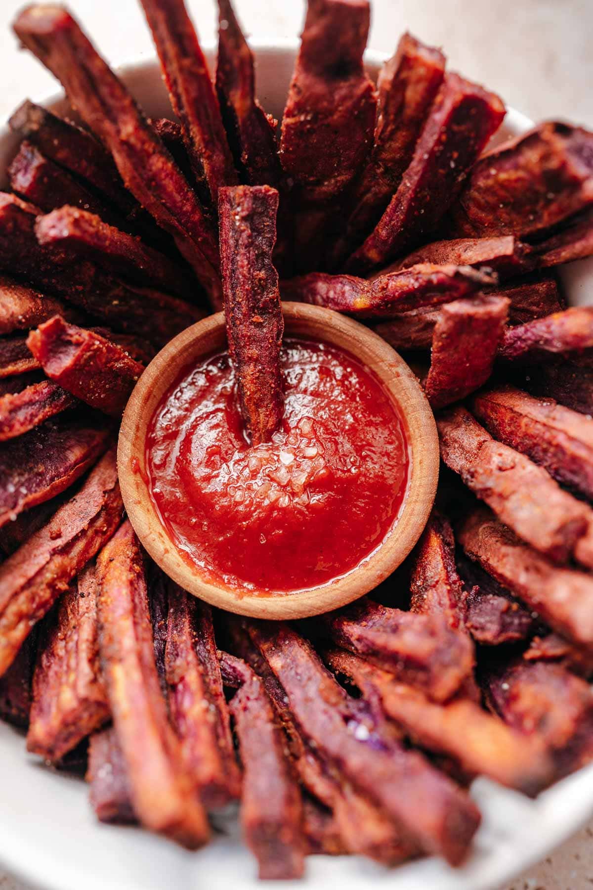 Close shot of a purple fry sticking out of a small wooden bowl of ketchup.