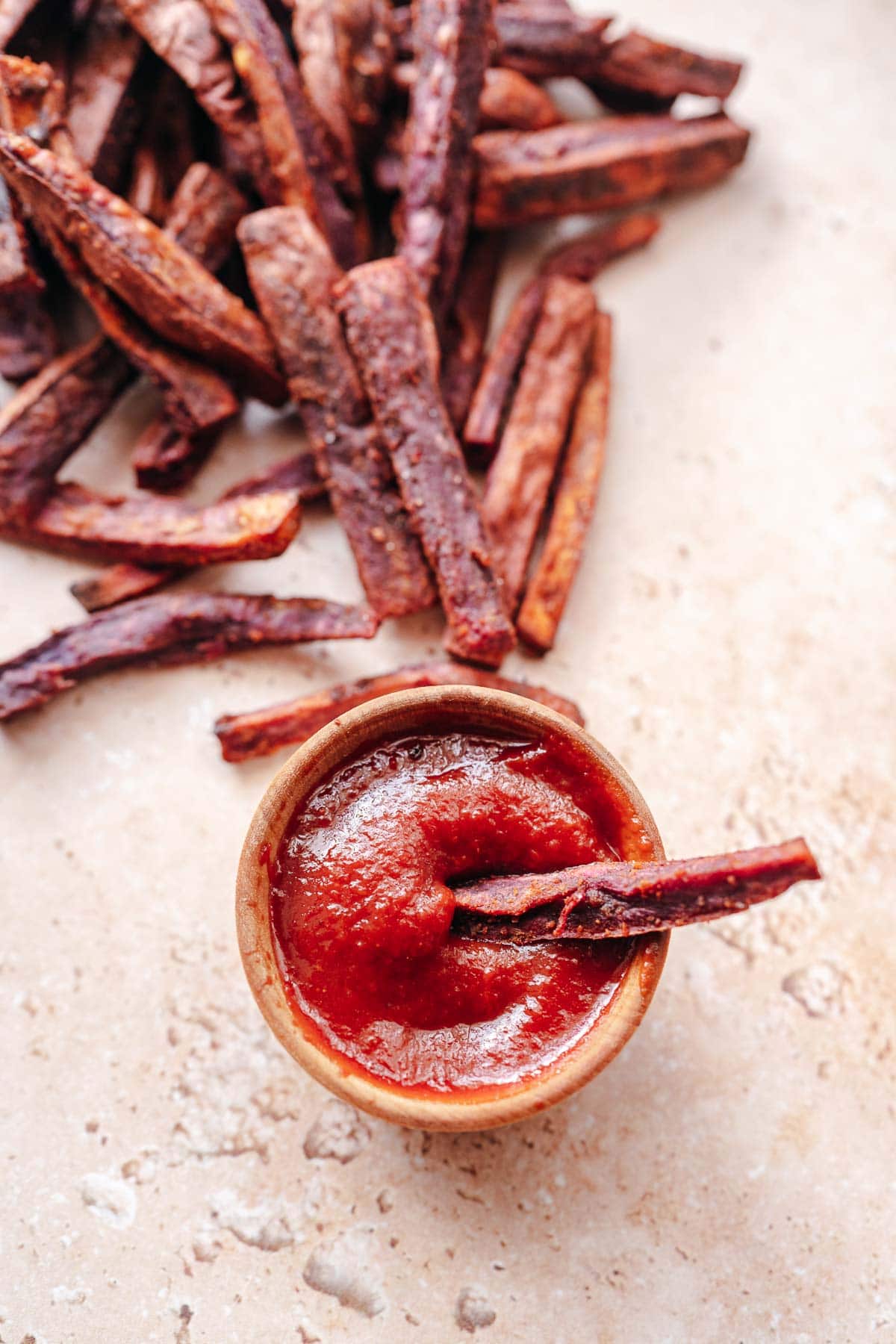 A purple fry in a small wood bowl of ketchup.