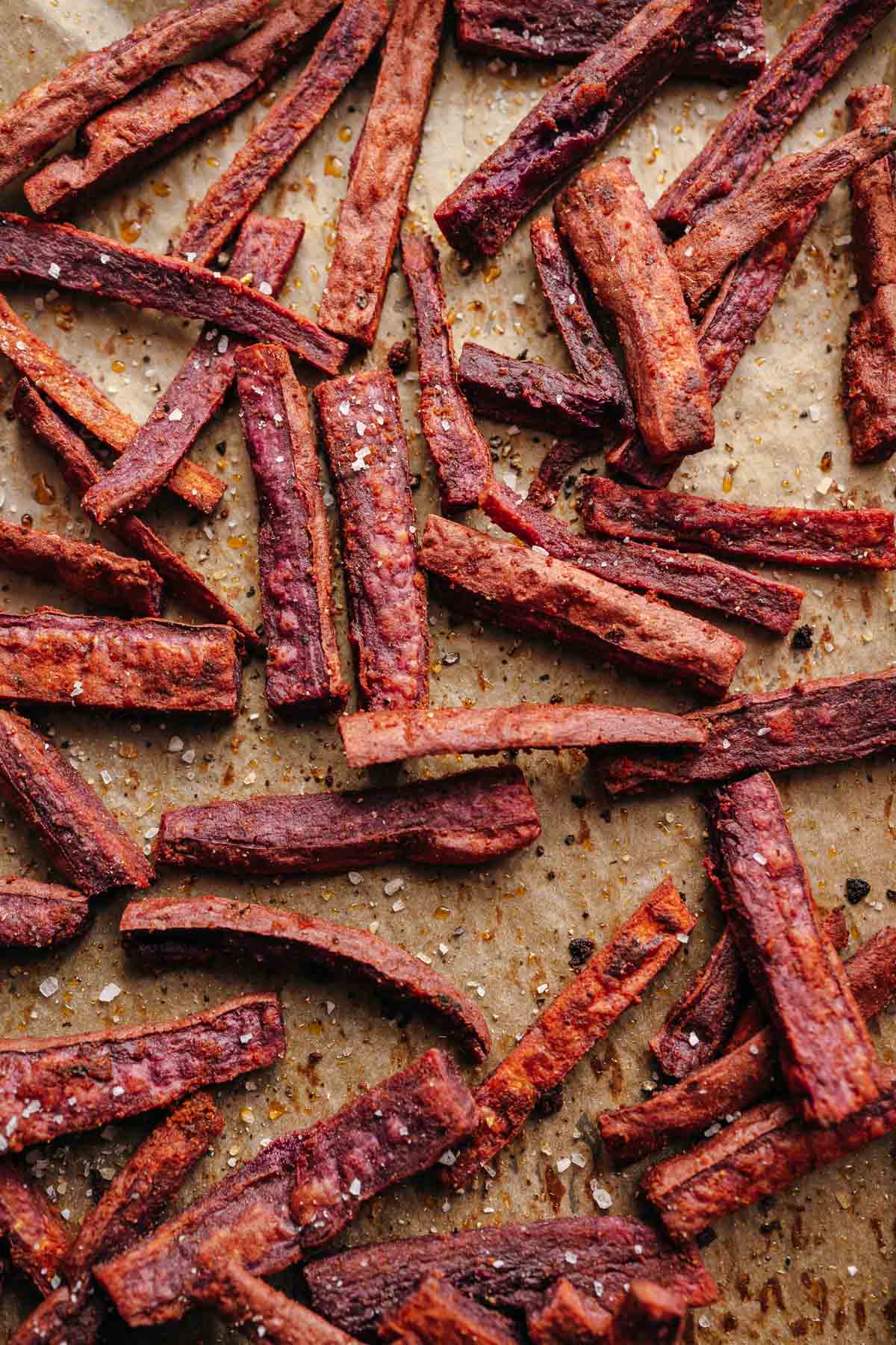 Parchment paper scattered with cooked purple fries sprinkled with salt.
