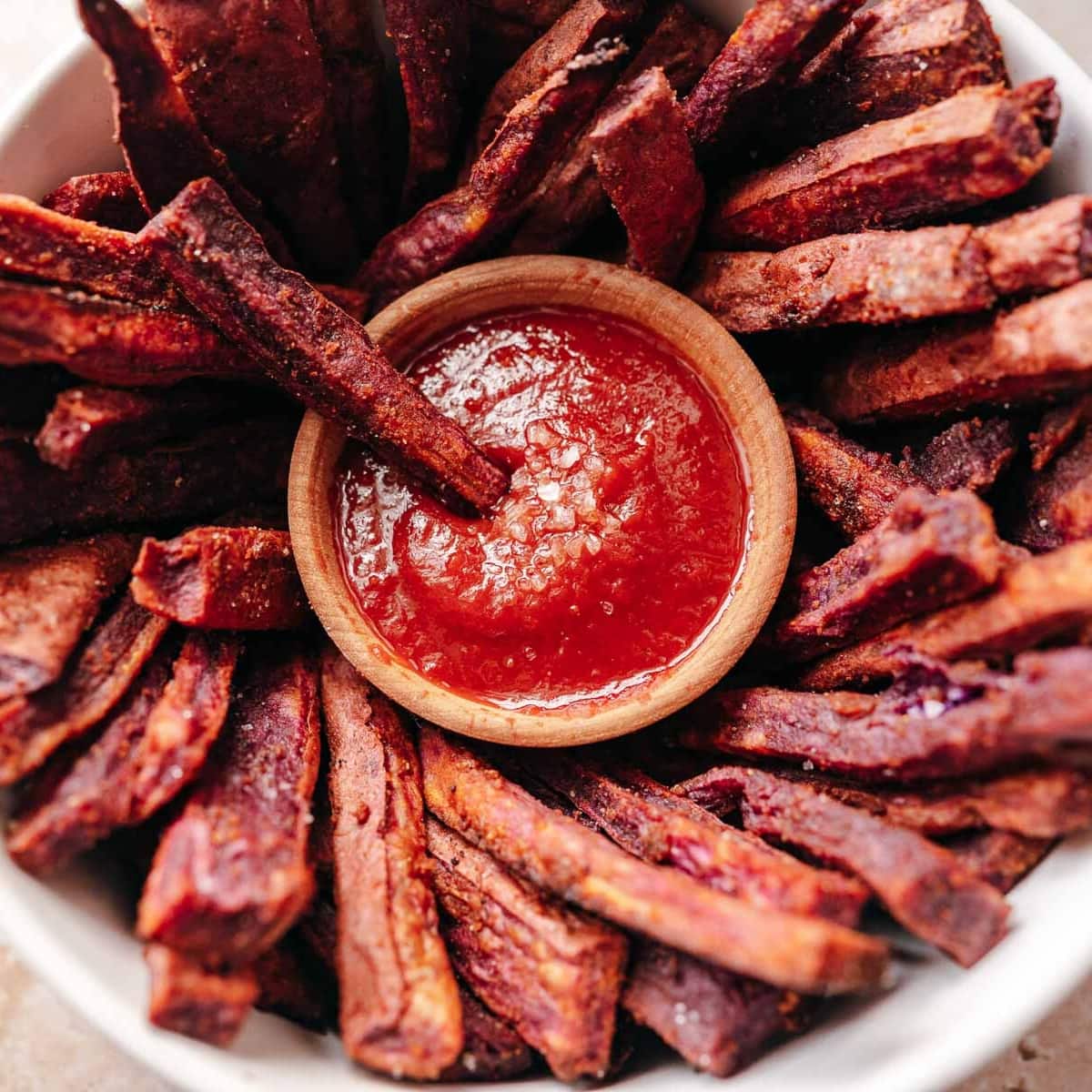 A close shot of a bowl of purple fries surrounding a small bowl of ketchup.