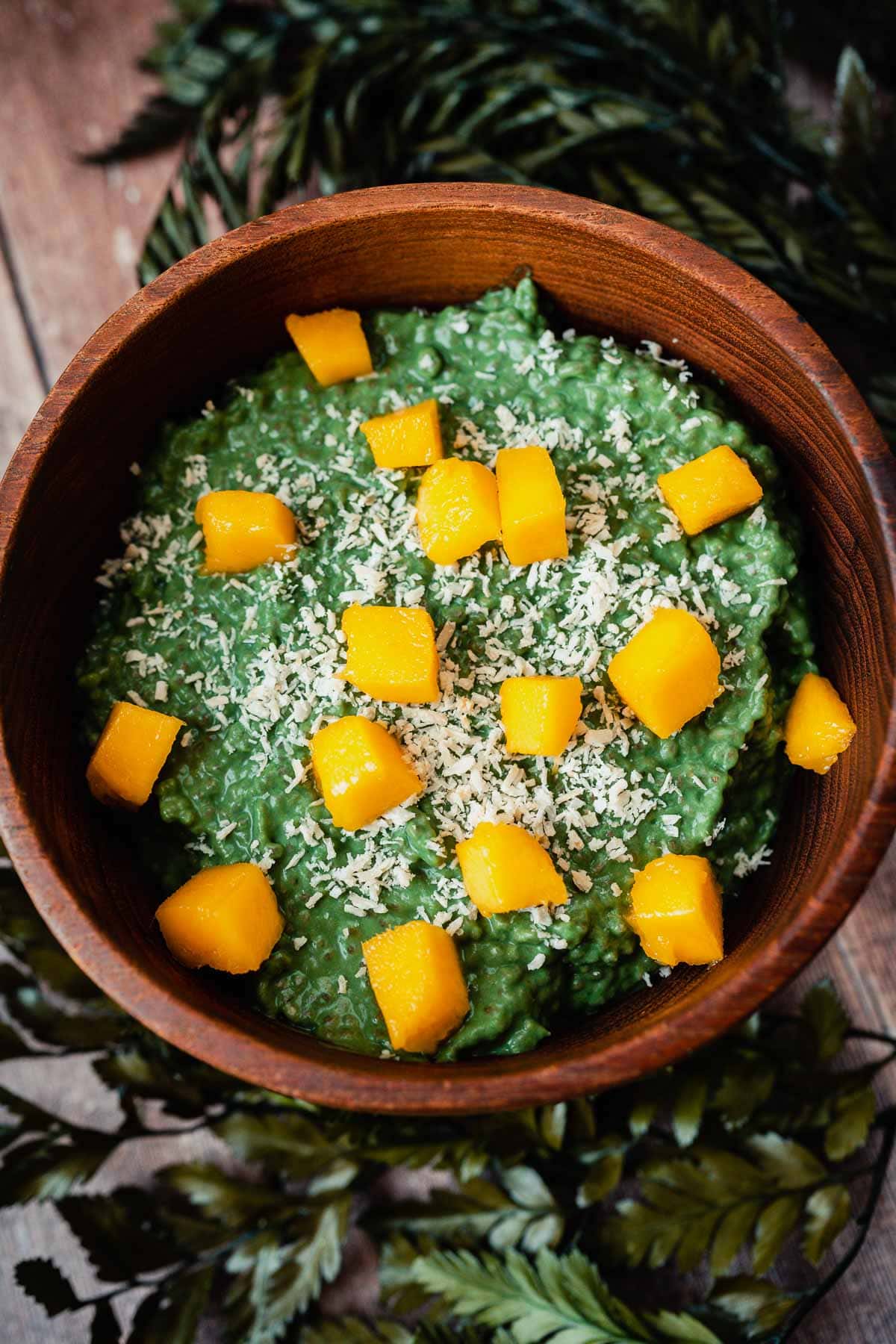 A dark wood bowl filled with green pudding and mango chunks.