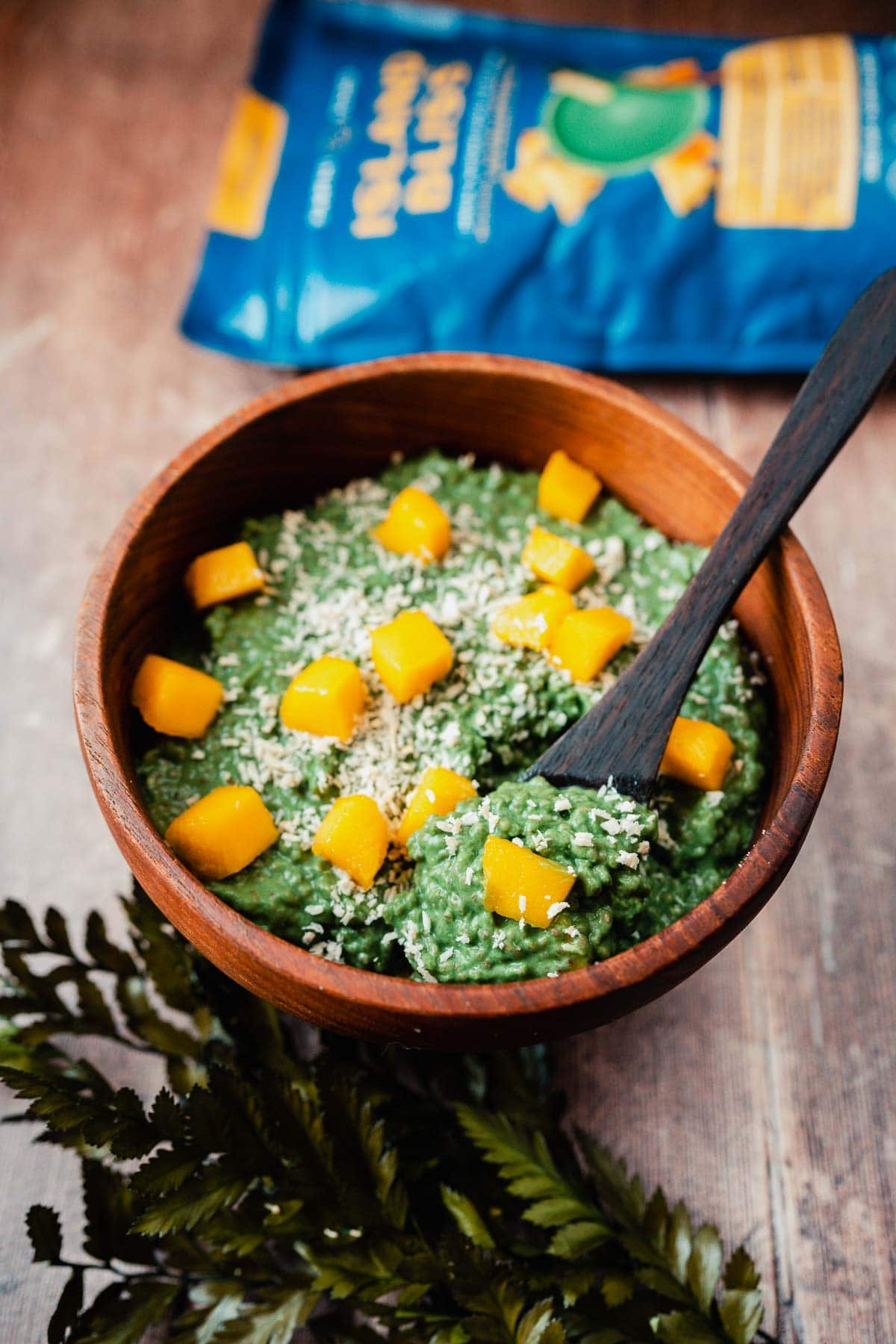 A wooden spoon sticking out of a wooden bowl of green tropical chia pudding.