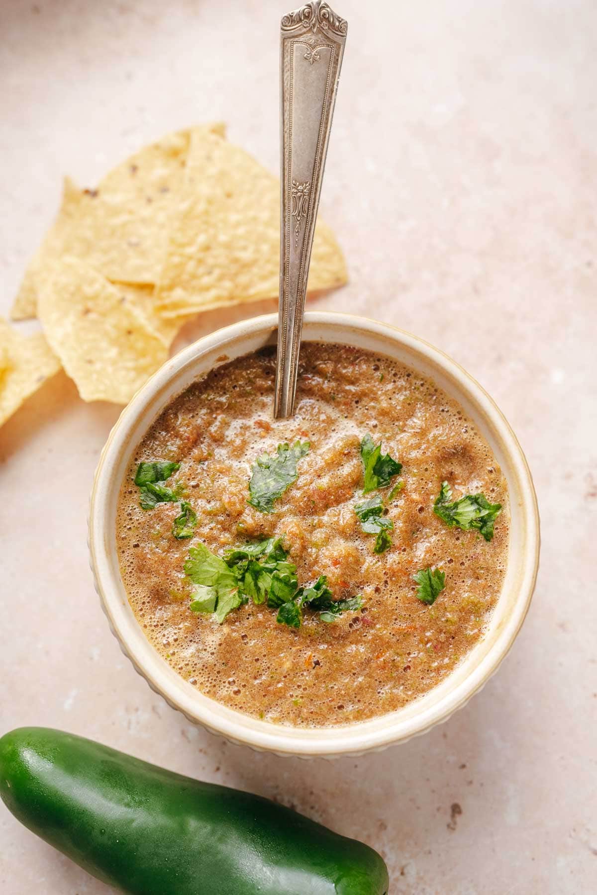 A large silver spoon jutting out of a small ceramic bowl filled with fresh charred salsa.