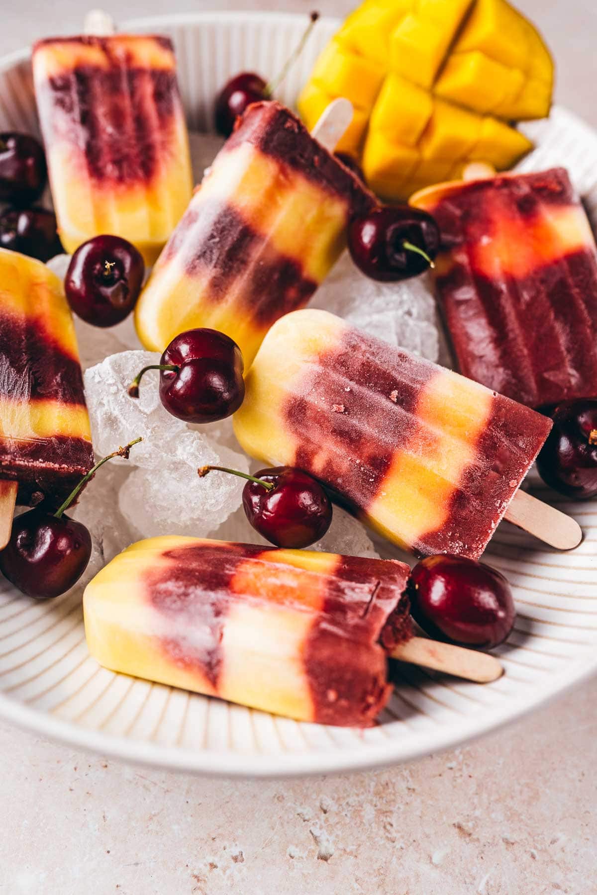 Close shot of mango cherry popsicles in a large ceramic bowl garnished with fresh cherries.