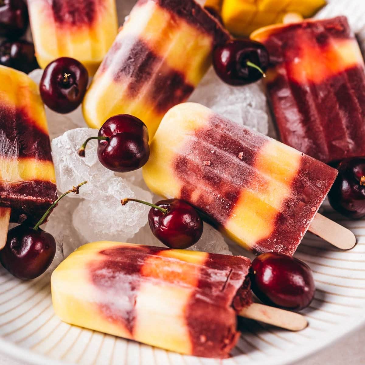 A stack of homemade cherry mango popsicles resting in a bowl of ice.