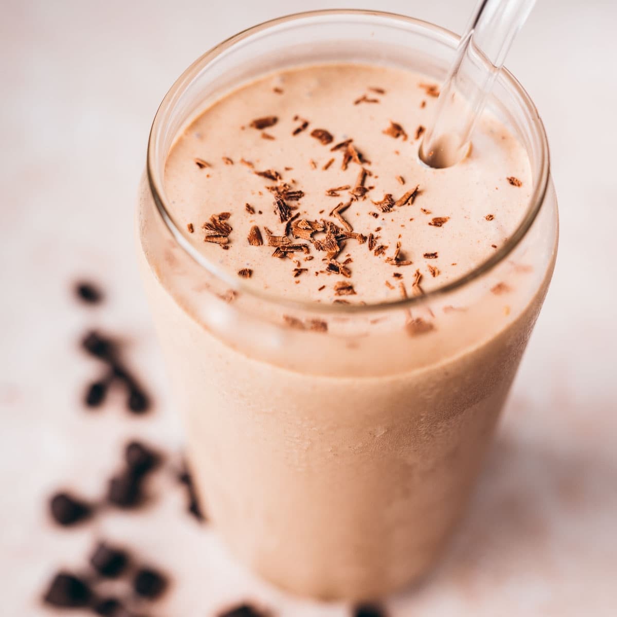 Close shot of a clear glass filled with light brown drink garnished with shaved chocolate.